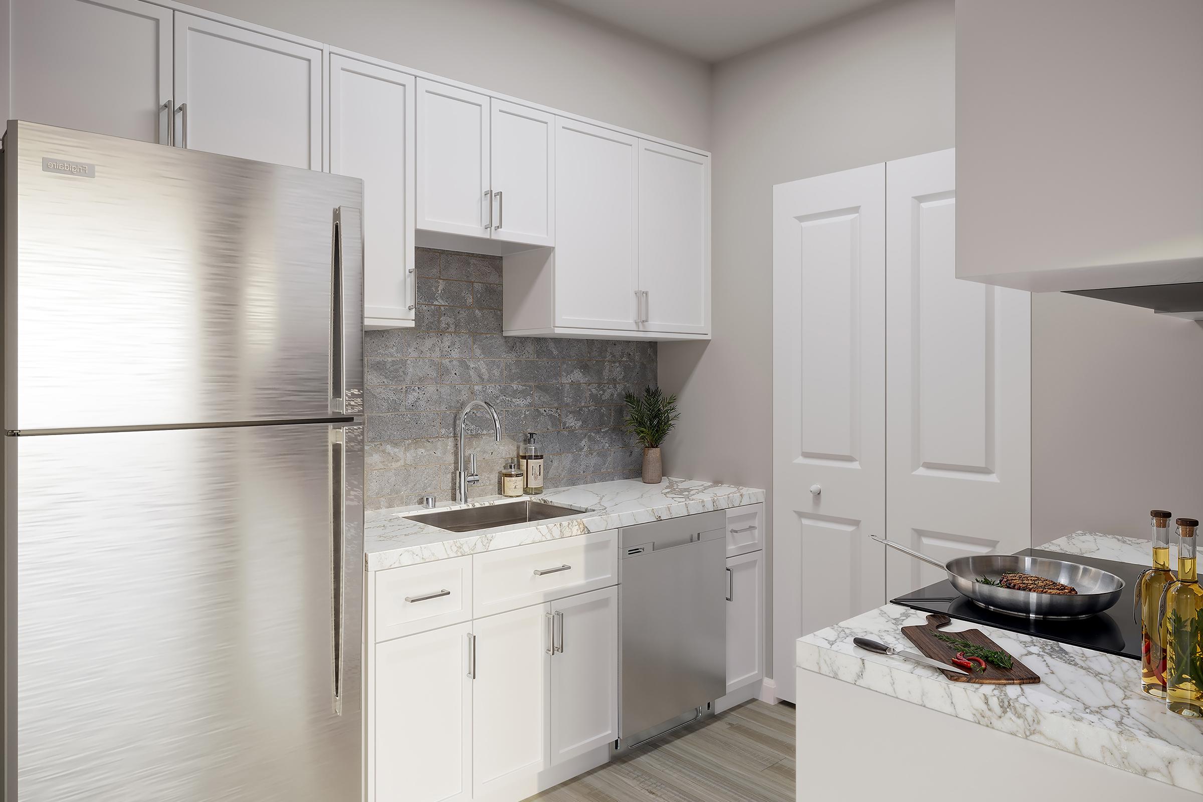 Modern kitchen featuring stainless steel appliances, including a refrigerator, and a sleek marble countertop. The cabinets are white, with a light backsplash adding elegance. A pot on the stove suggests cooking activity, while a small plant adds a touch of greenery to the space.
