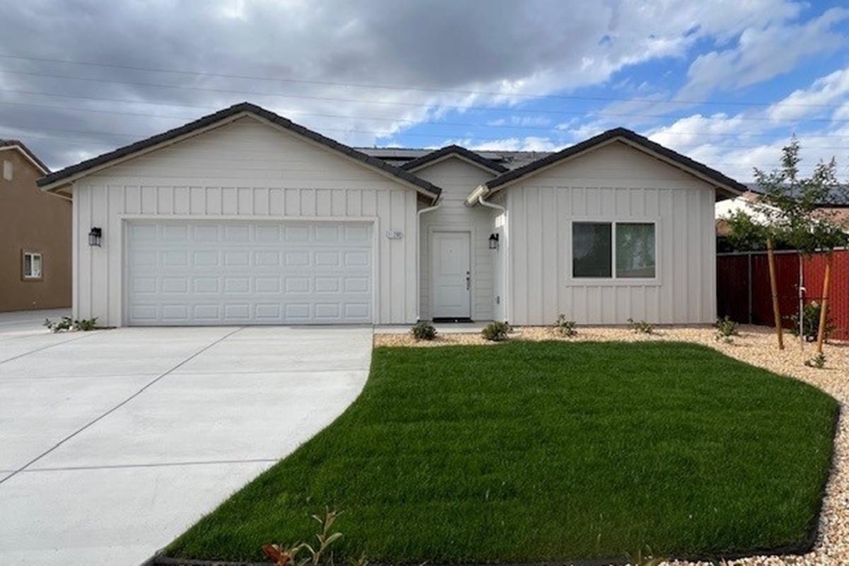 A modern single-story house with a light-colored exterior, a two-car garage, and a neatly landscaped front yard featuring green grass and decorative gravel. The sky above is partly cloudy, adding a fresh atmosphere to the scene.
