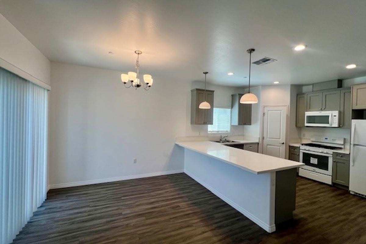 Spacious modern kitchen and dining area featuring a large island with bar seating, pendant lighting, and white cabinetry. The room has wooden flooring, large windows for natural light, and is designed in neutral colors to create an inviting atmosphere.