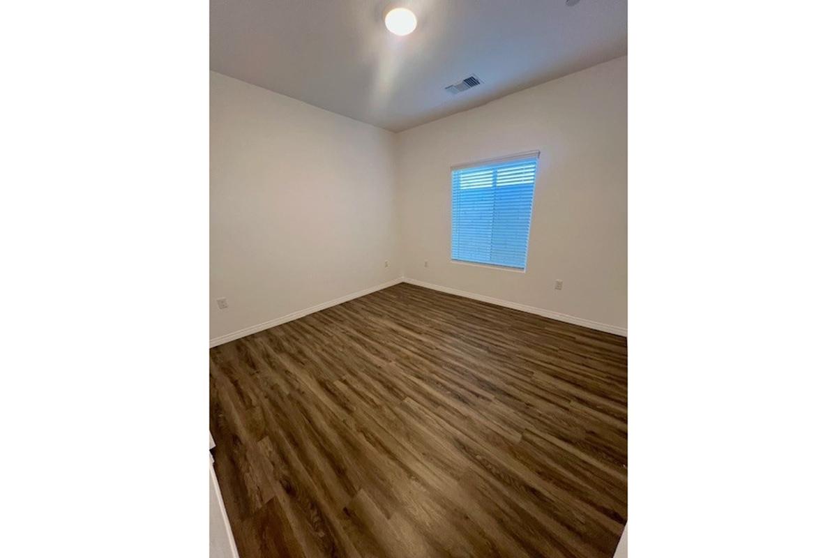 Empty room with light-colored walls and hardwood flooring. A window with white blinds is on the left side, allowing natural light to enter. The ceiling has a round light fixture, and the space appears clean and well-maintained, suitable for various uses.