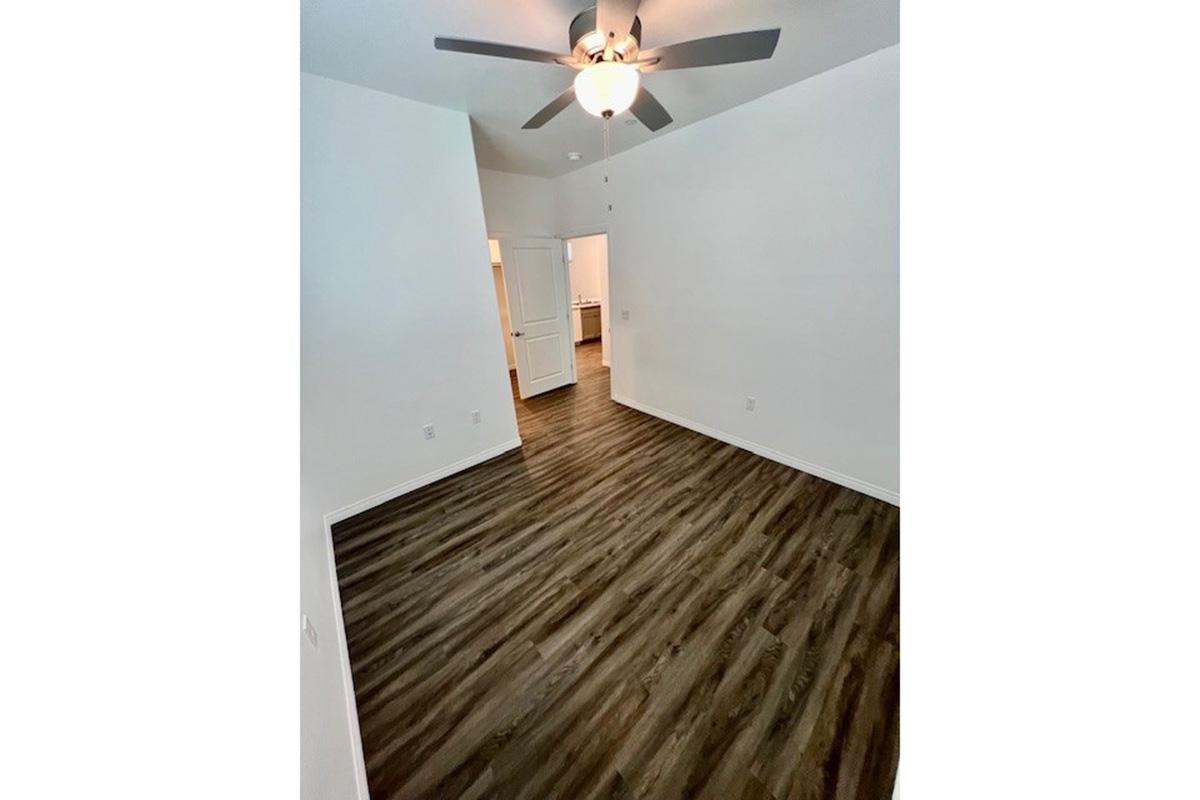 Spacious room featuring wood laminate flooring, a ceiling fan, and a neutral color palette. The doorway in the background leads to another area, and the overall space is well-lit and inviting. Ideal for various uses such as a living room, bedroom, or office.