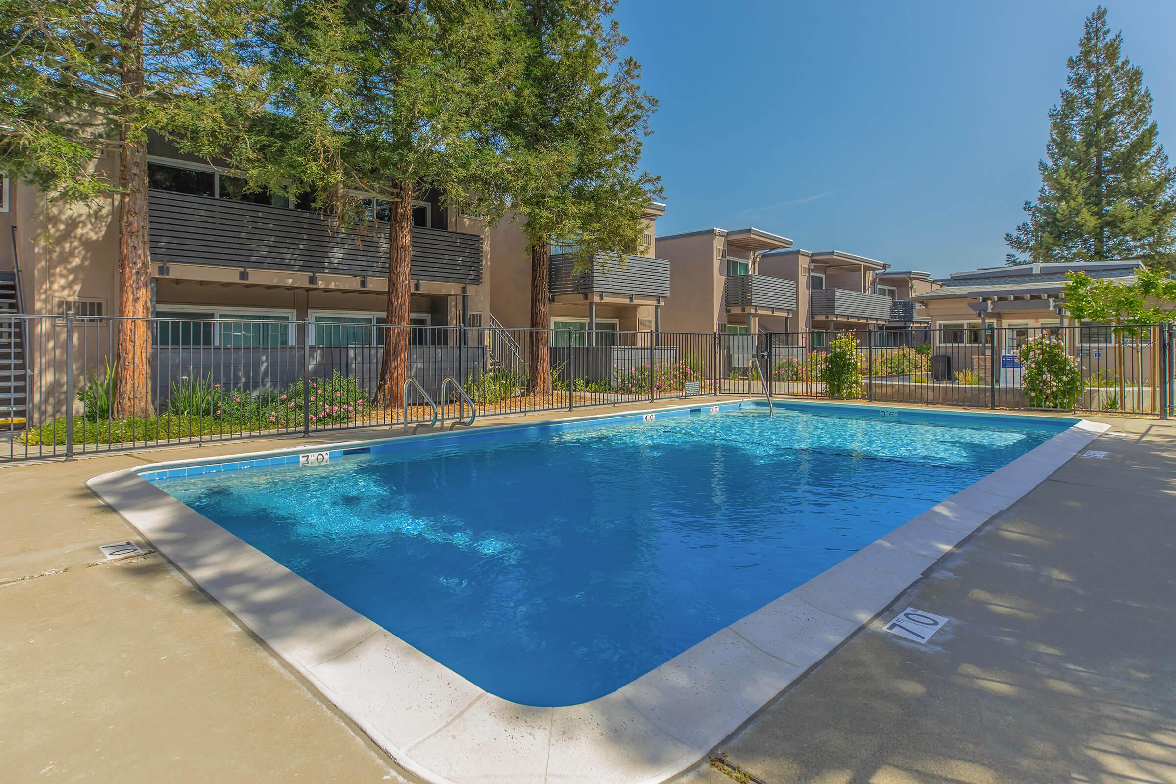 Blue swimming pool with apartments and trees.