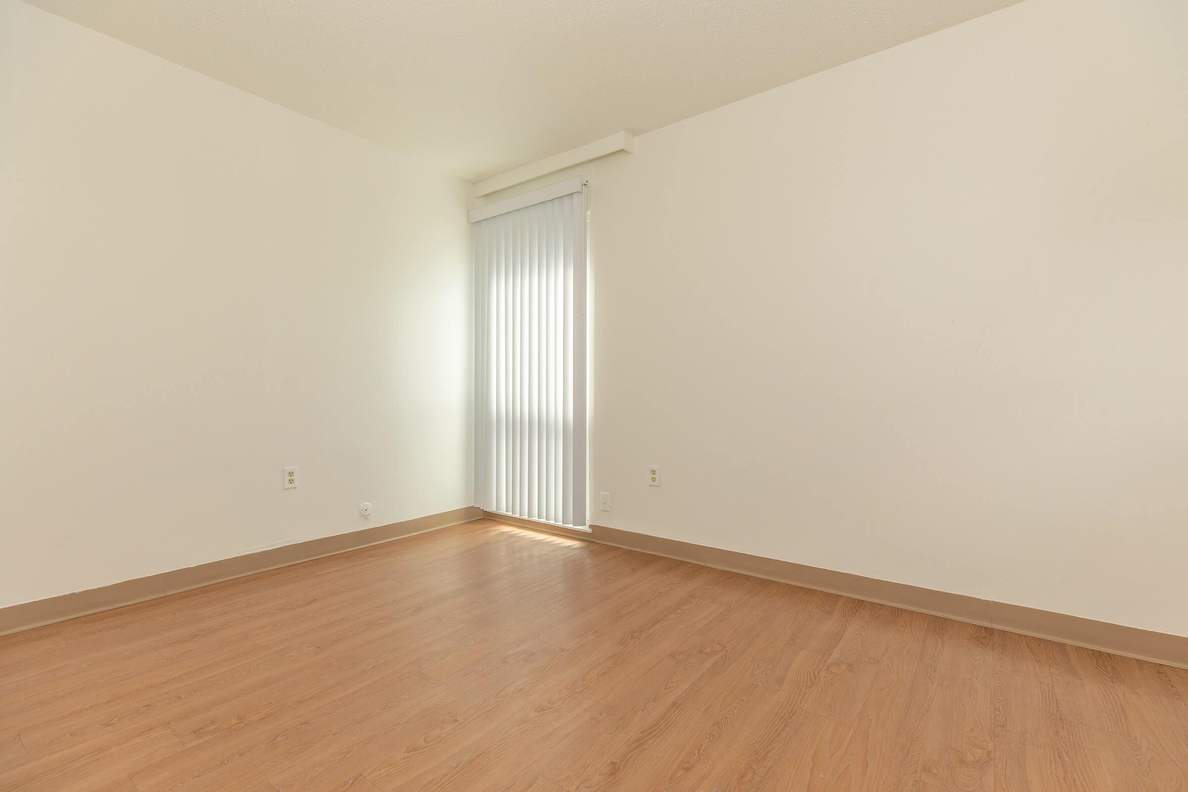 Bedroom with white walls, hardwood floors, and a tall window with vertical blinds.