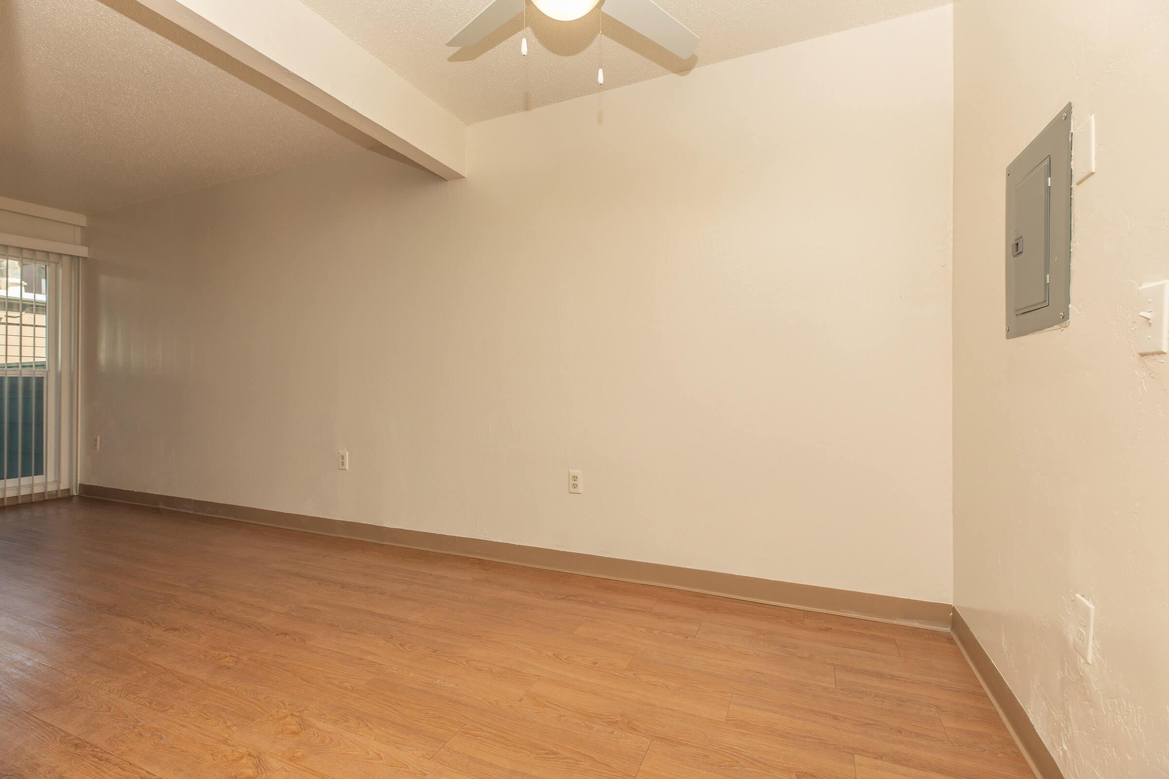 Dining area with white walls, hardwood floors, ceiling fan, and breaker box on wall.