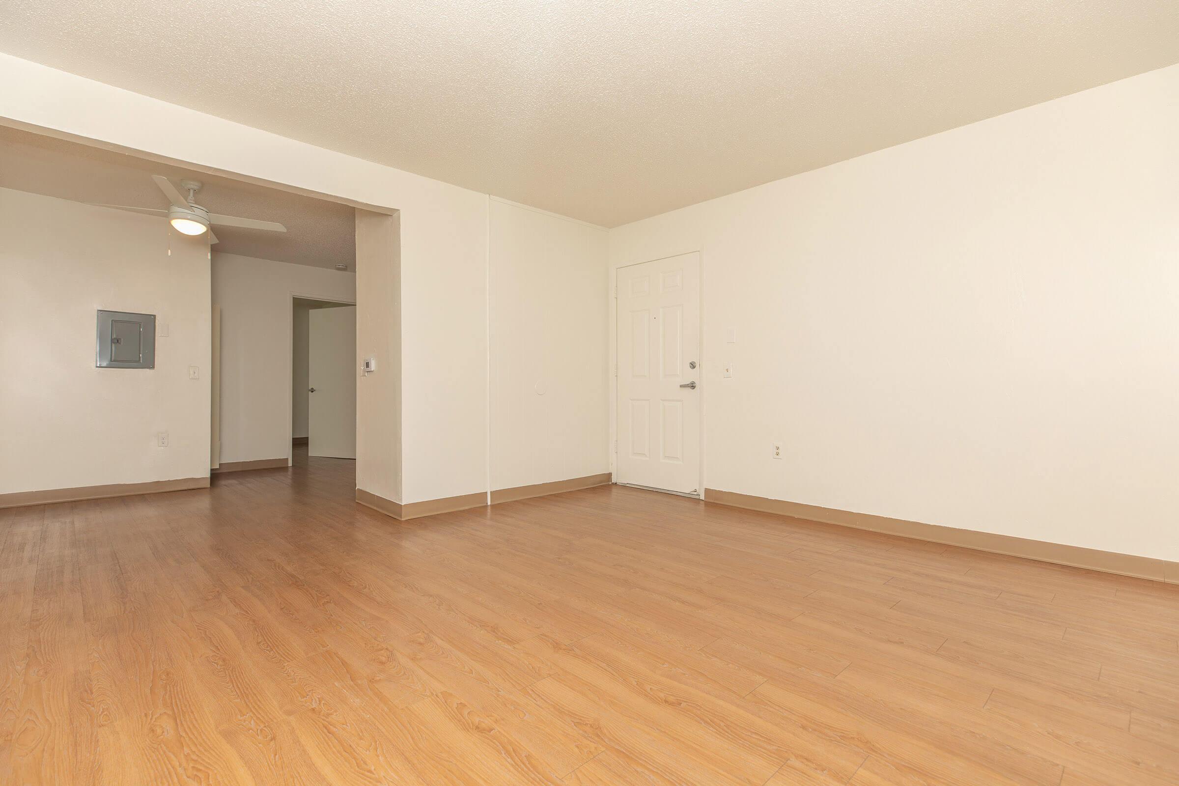 One bedroom apartment living room with white walls and hardwood flooring, with view into hallway.