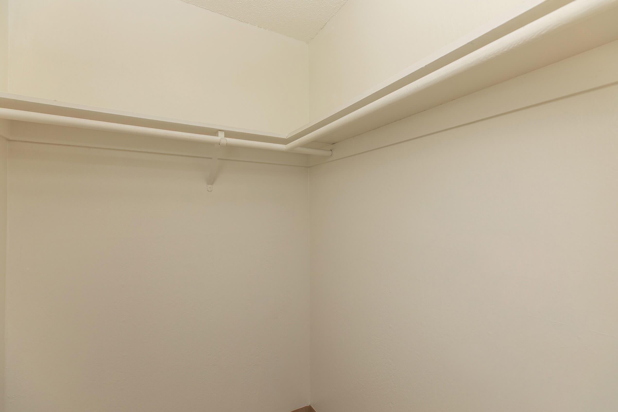 Walk in closet with white closet bars and shelf space on white walls.