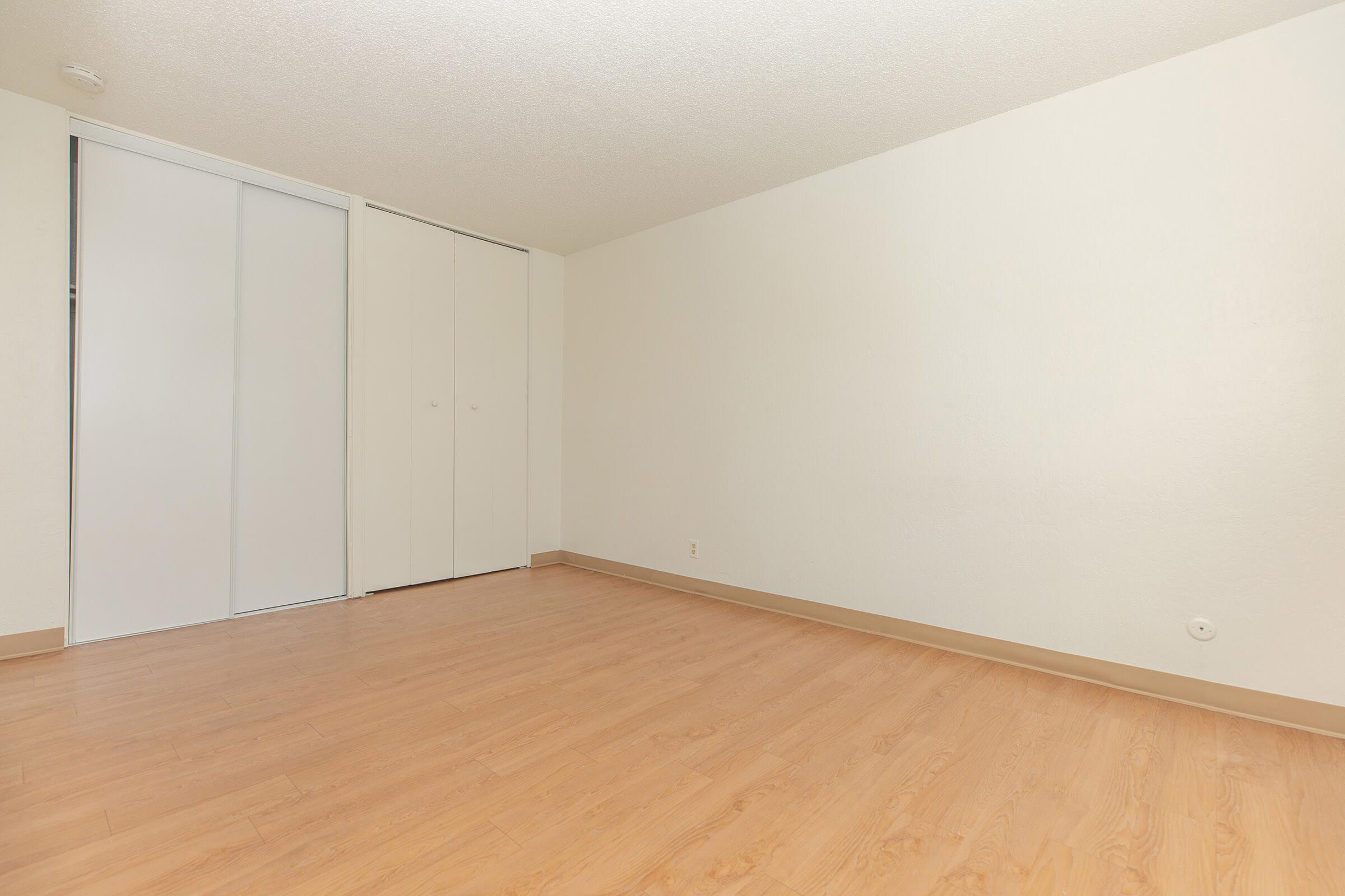 Bedroom with closed closet doors, white walls, and hardwood floors.