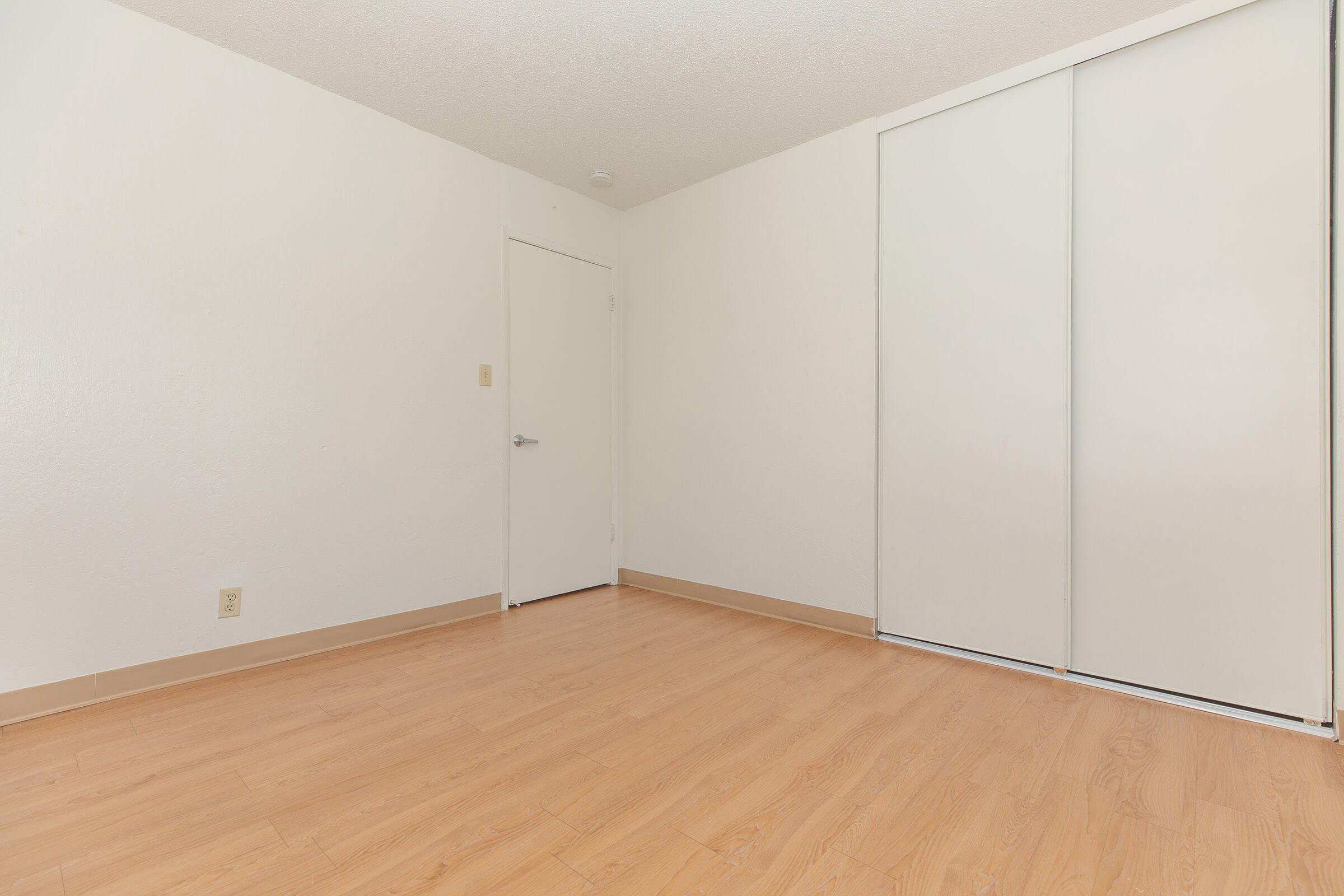 Closed bedroom closet, with white walls, hardwood floors, and the main bedroom door.