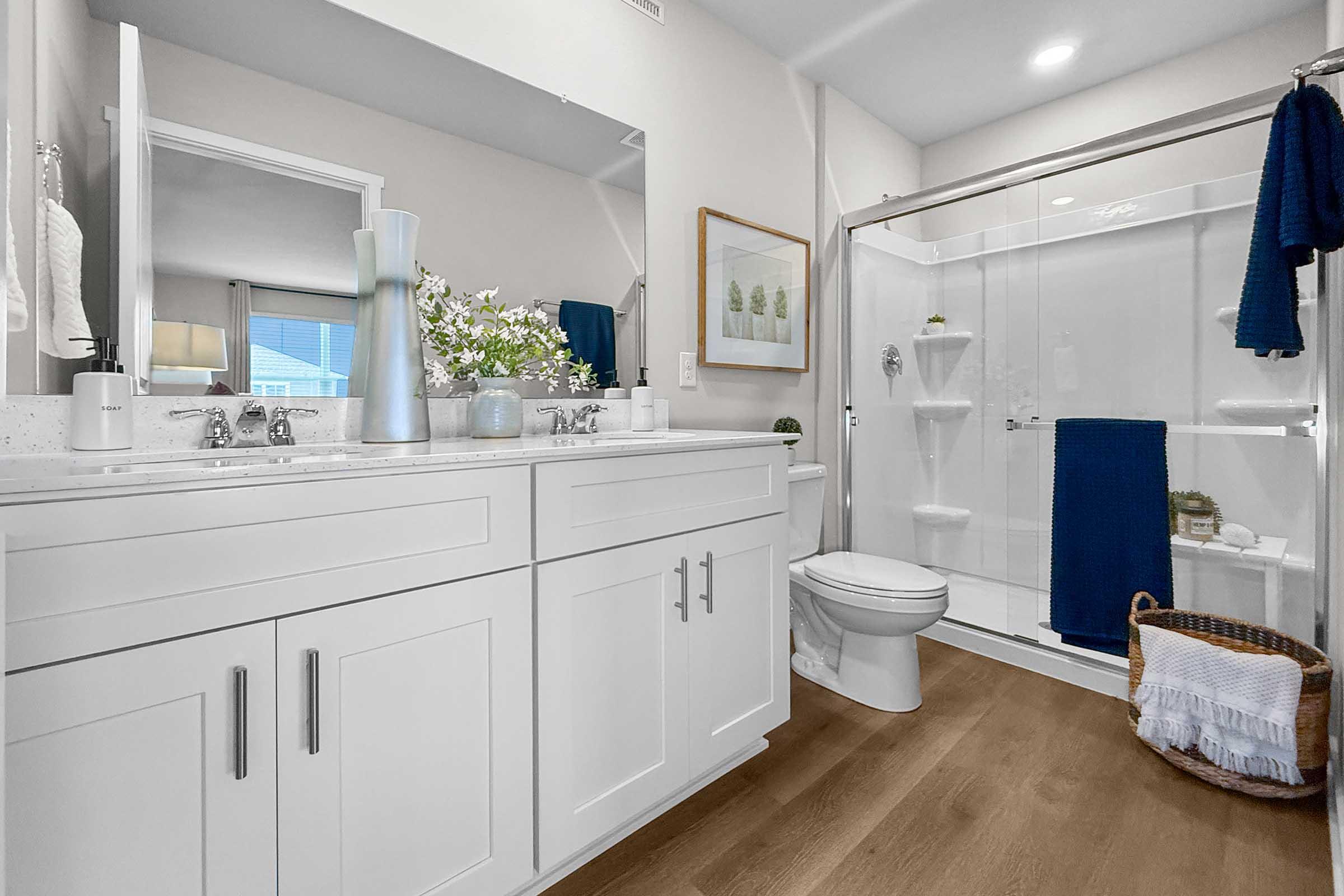 Modern bathroom with quartz countertops, glass shower, and wood-style flooring in Painted Woods Villas three-bedroom townhome.