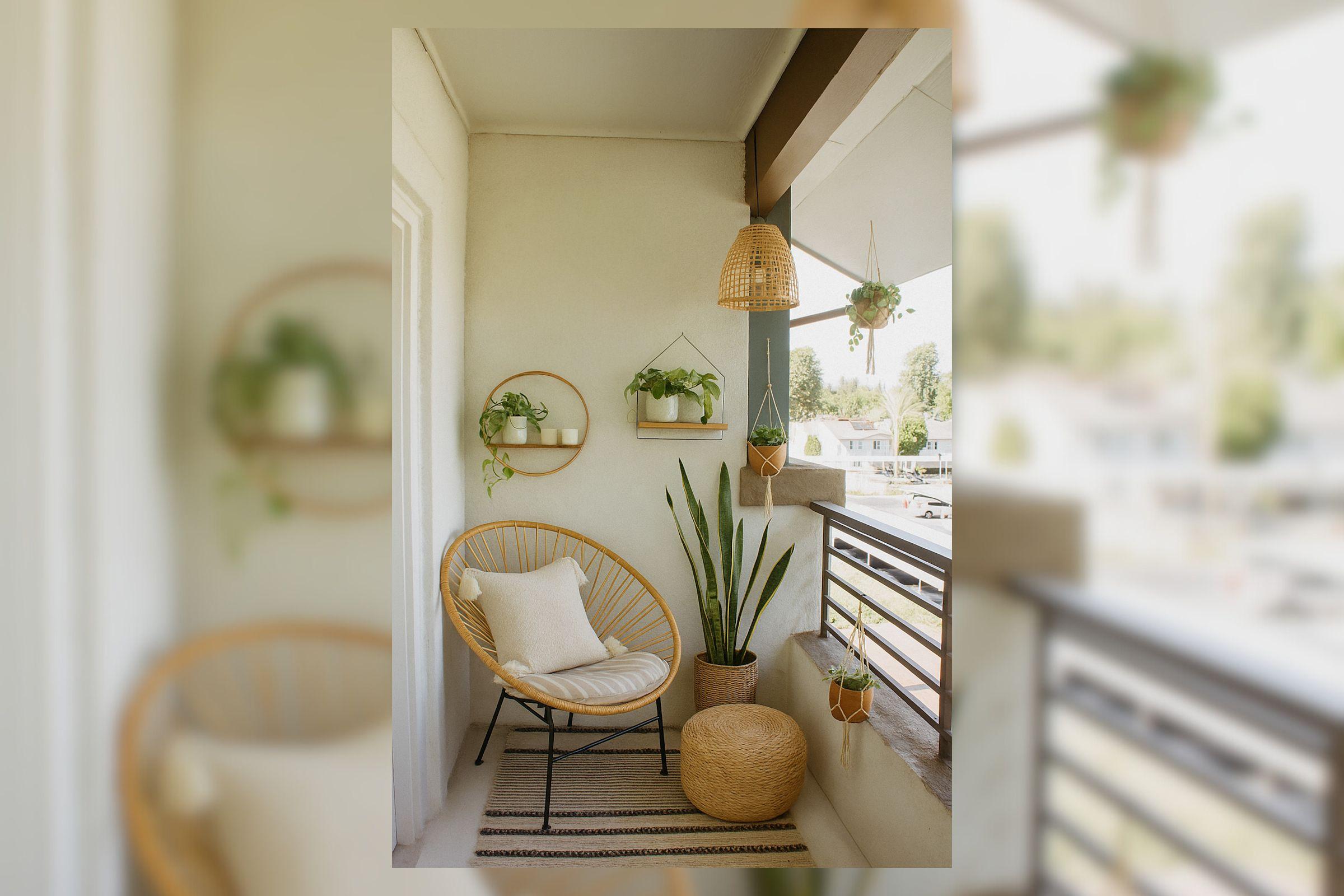 A cozy balcony with a rattan chair and a light cushion, surrounded by potted plants on wall shelves and hanging planters. A woven basket sits nearby, with a textured rug underfoot. The scene creates a serene and inviting atmosphere with natural light streaming in.