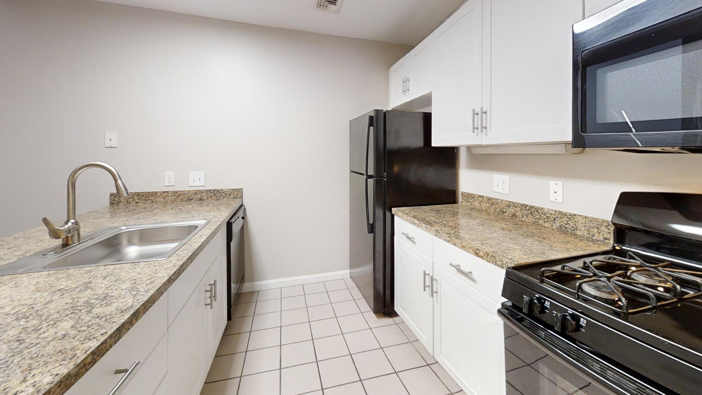 Modern kitchen featuring white cabinets, granite countertops, stainless steel sink, and black appliances, including a refrigerator and a stove. The floor is tiled, and the walls are painted a light color, providing a clean and contemporary look.