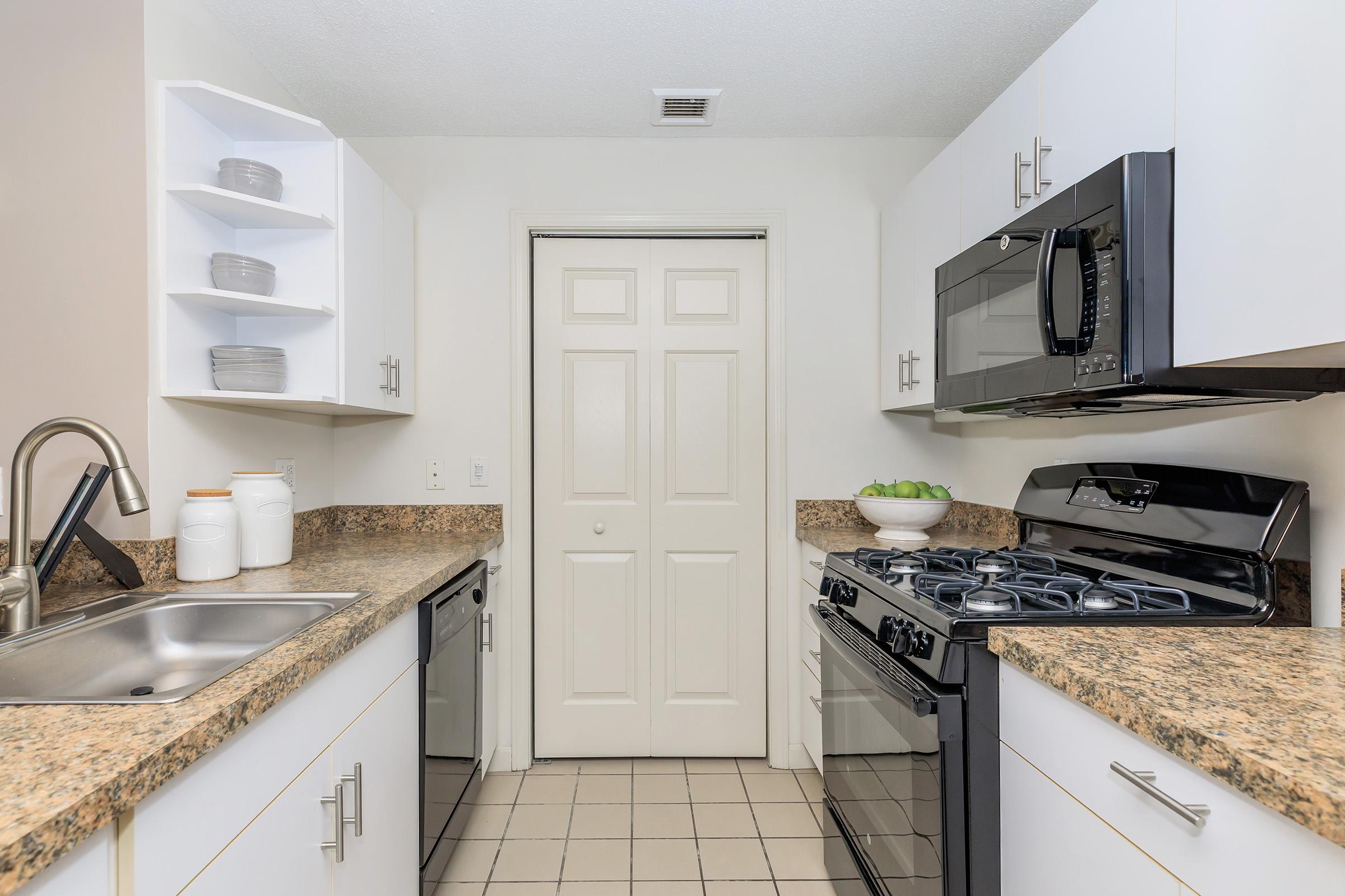 Dog-Friendly Apartments in Manchester CT - The Manchester - Galley Kitchen With White Cabinets, Granite Look Counters, Stainless Microwave, Gas Range, Double Sink, And Tile Floor