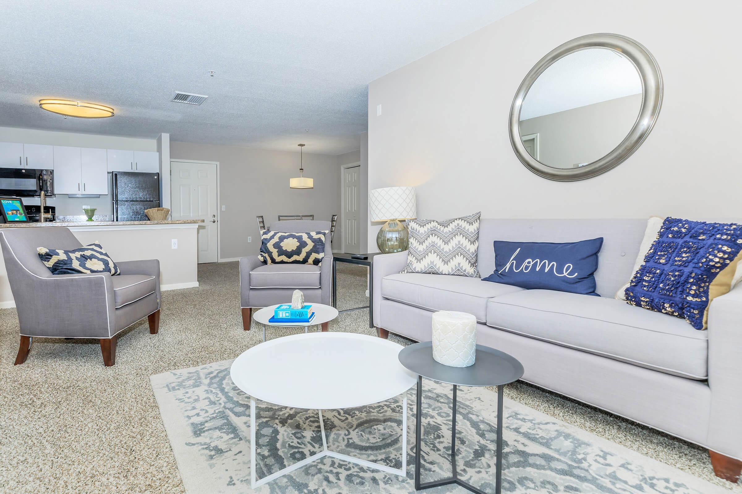Manchester CT Apartments for Rent - The Manchester - Open Concept Living Room With Plush Sofa, Accent Chairs, Round Coffee Table, And View Into White Kitchen With Breakfast Bar