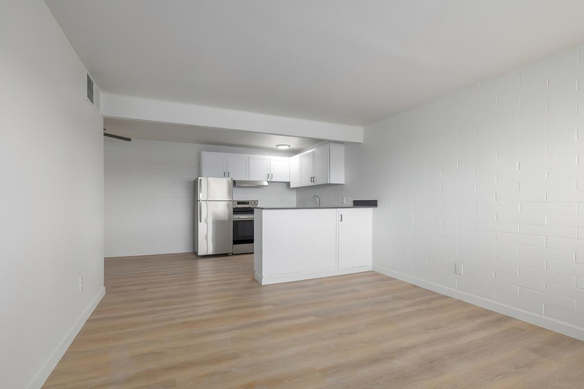 Modern kitchen and living space featuring white cabinets, stainless steel appliances, and light wood flooring. The room has a minimalist design with a bright, open layout and clean lines, enhancing the spacious atmosphere.