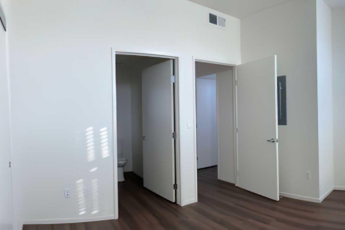 A well-lit interior space featuring two partially open doors. One door leads to a small bathroom, while the other opens to an adjacent area.