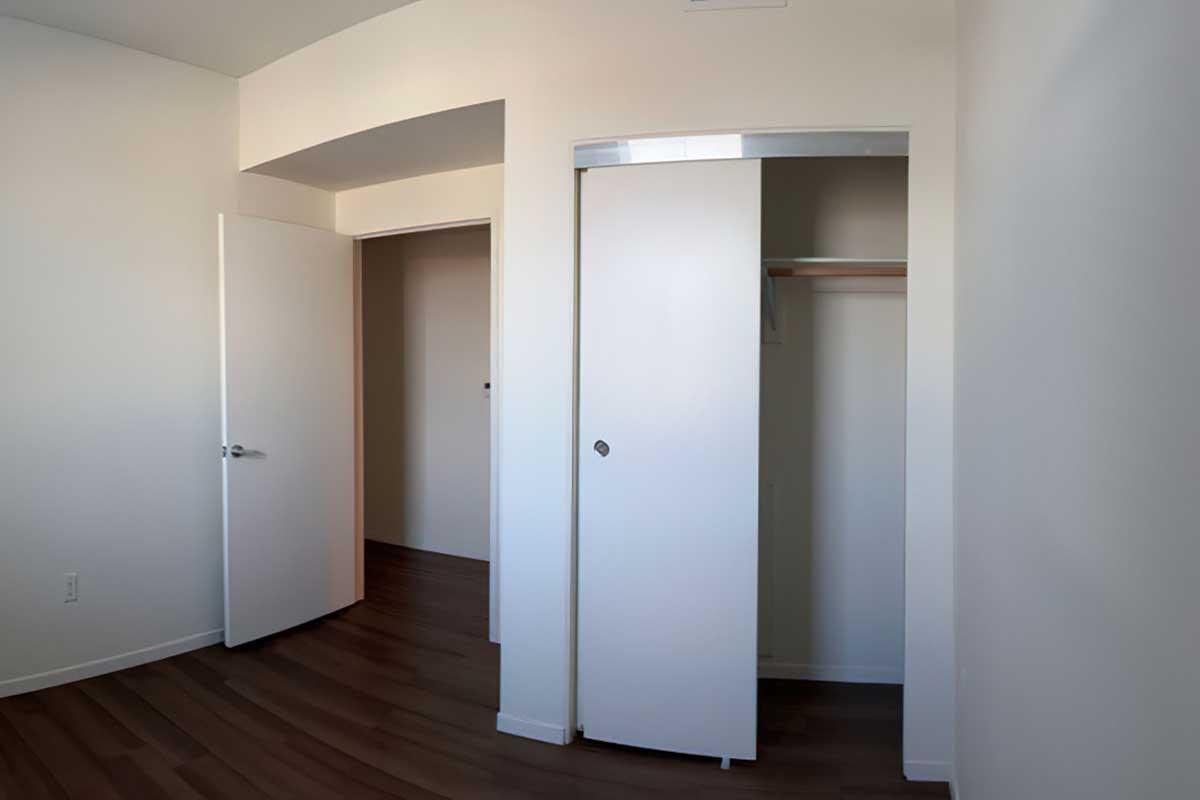 A well-lit, empty room featuring light-colored walls and dark wood flooring.