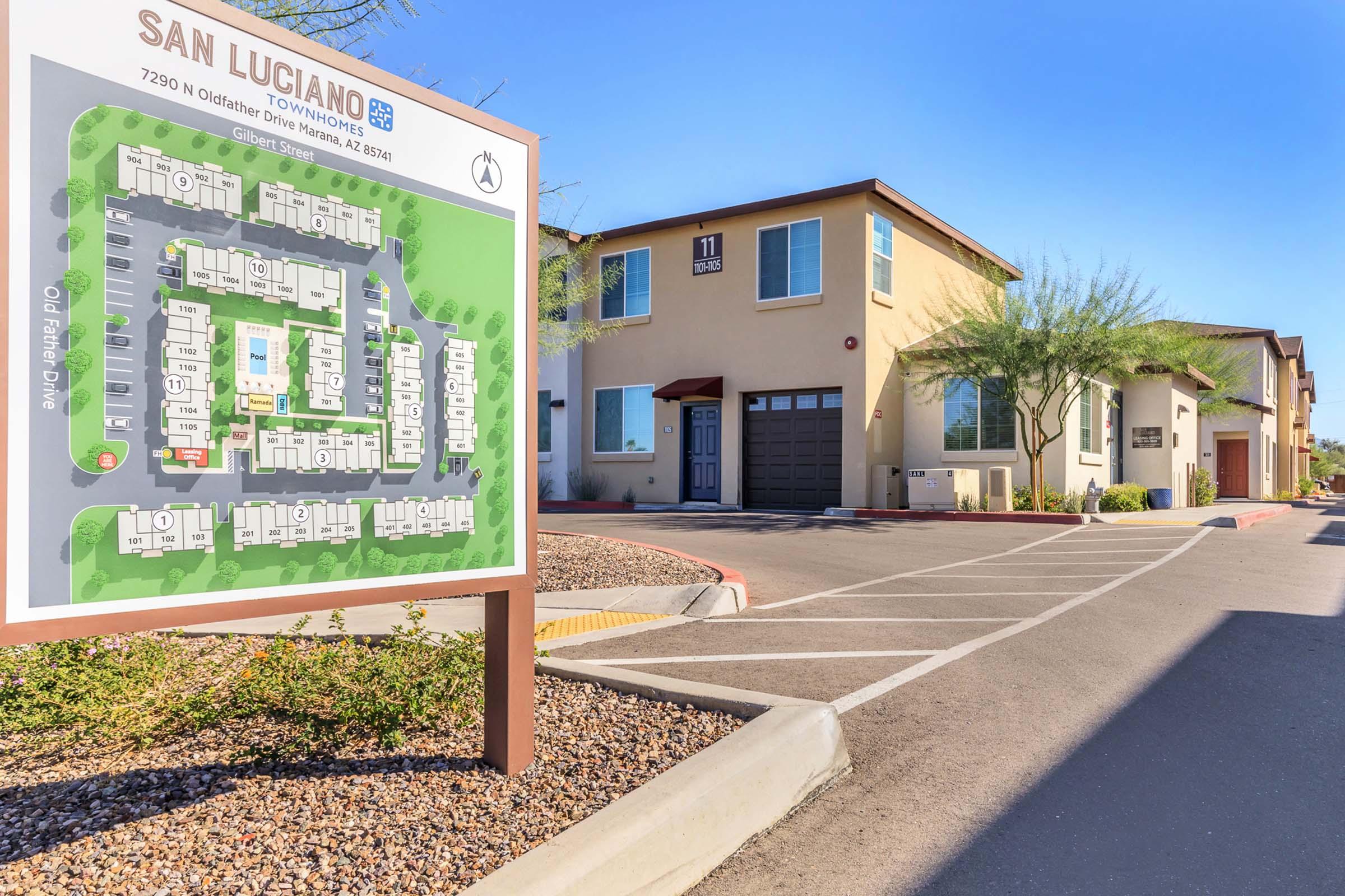 A sign displaying the layout of San Luciano Townhomes, located at 7290 N Oakstone Drive, Tucson, AZ. The map includes details of the community layout, highlighting parking areas and individual townhome units, with a sunny sky and landscaped surroundings in the background.