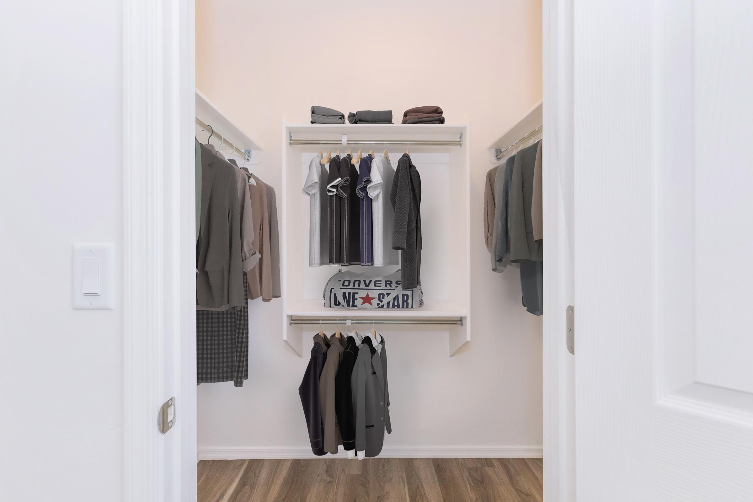 A neatly organized closet featuring a variety of clothing items. Shelves hold folded clothes, while several shirts and jackets are hanging on racks. The closet has a light color scheme and wooden flooring, creating a clean and spacious appearance.
