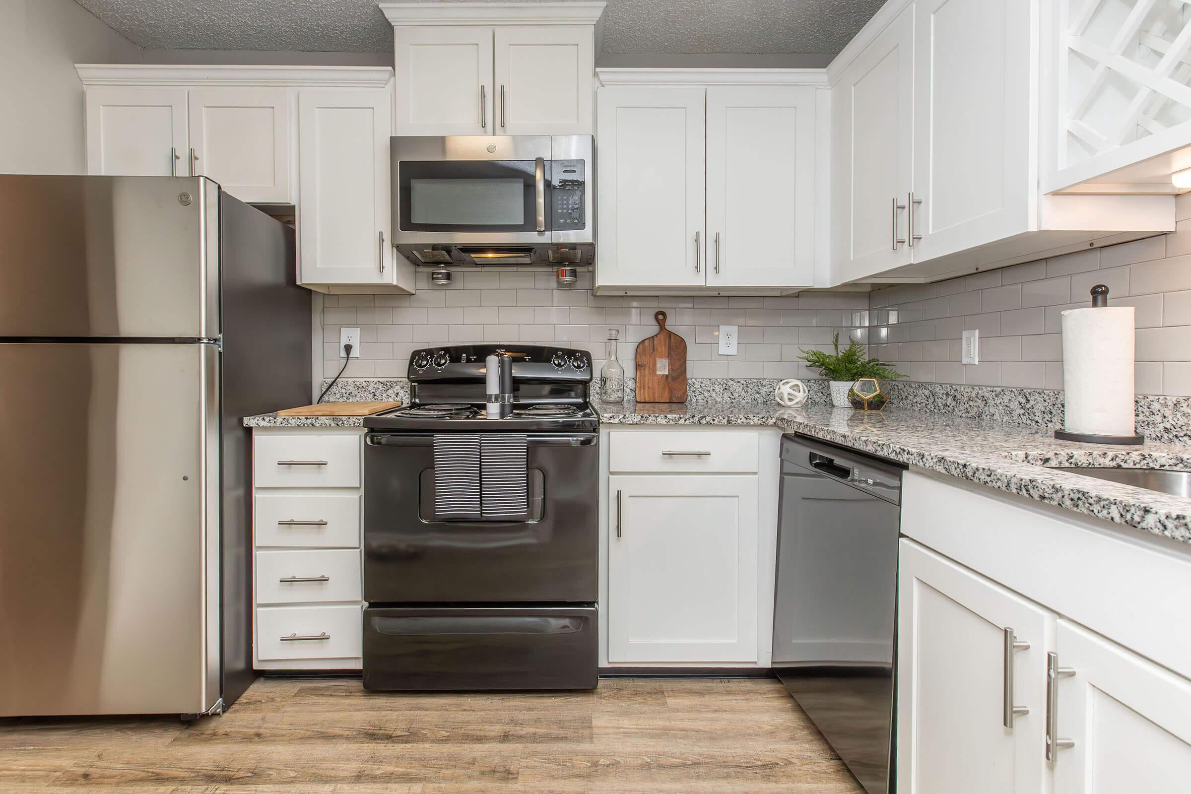 Modern kitchen featuring white cabinets, stainless steel appliances including a refrigerator and microwave, a black stove, and a dishwasher. The countertop is granite with a subtle pattern, and there are decorative items and kitchen essentials on display, creating a clean and inviting atmosphere.
