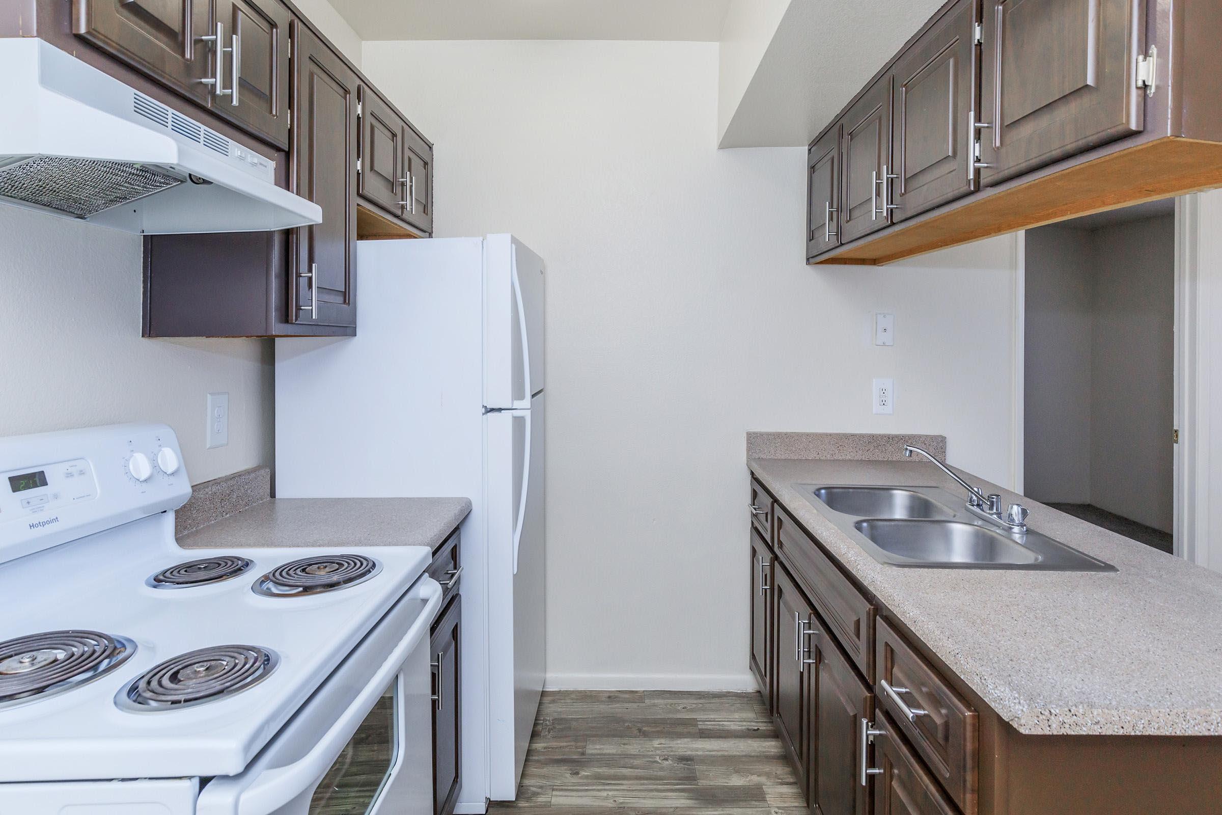 A modern kitchen featuring white appliances, including a stove and refrigerator, with dark wood cabinets above and a countertop space. The kitchen has a double sink and a neutral-colored wall, creating a clean and bright atmosphere.