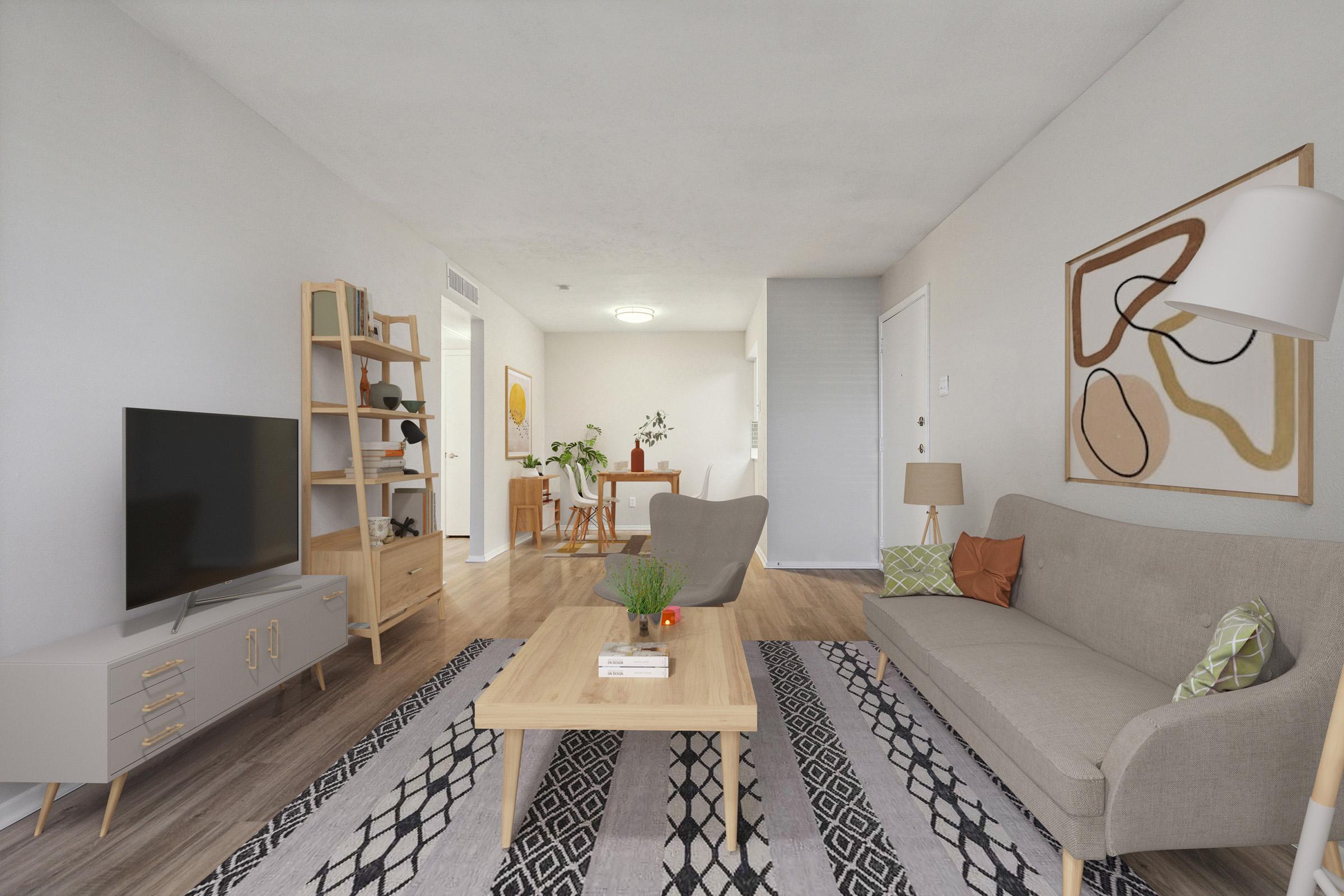 A modern living room featuring a light gray sofa with decorative pillows, a wooden coffee table, and a patterned area rug. There's a TV on a stylish console, a bookshelf, and a floor lamp. The background shows a dining area with a small table and chairs, creating a warm, inviting atmosphere.