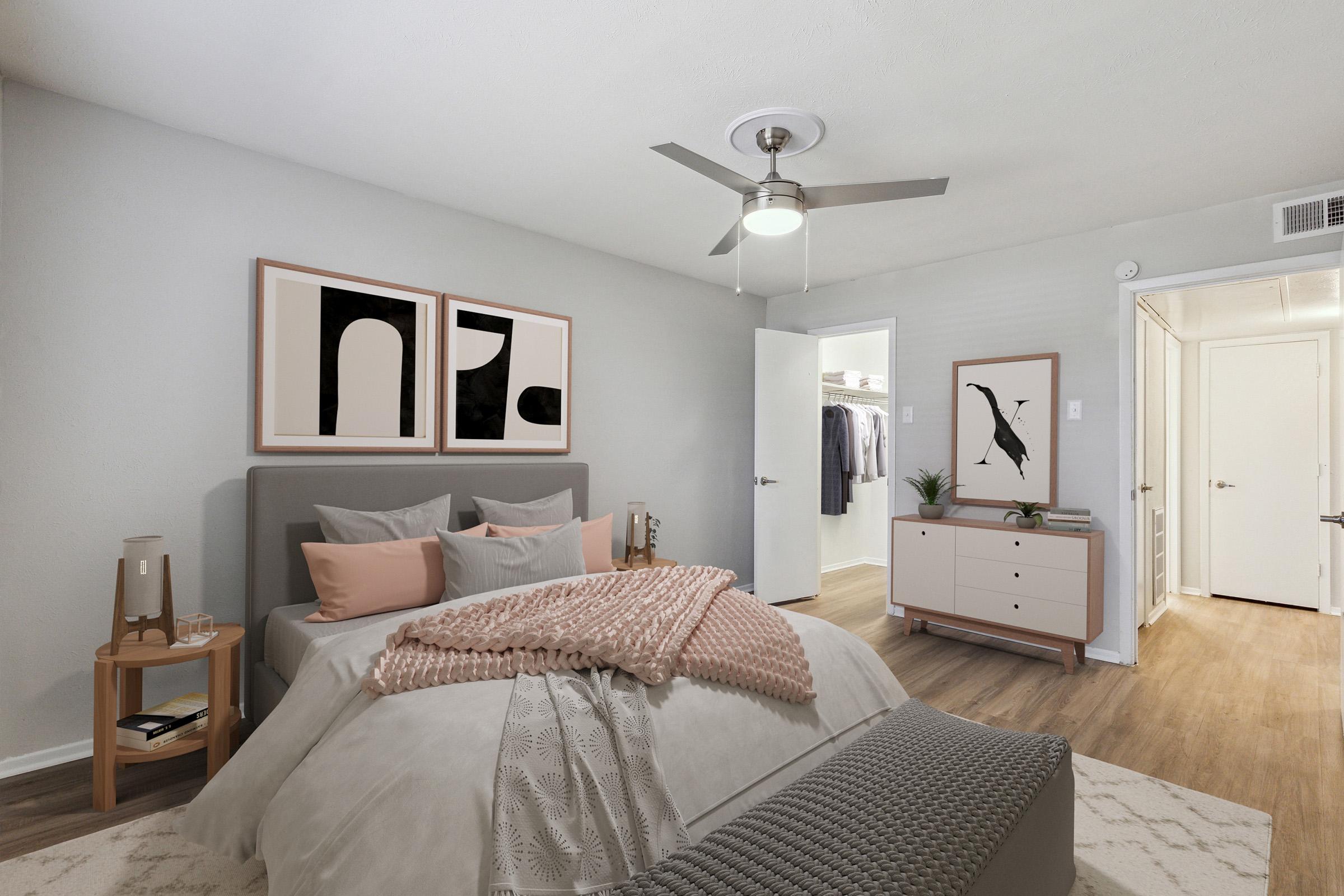 A modern bedroom featuring a gray and beige color scheme. The bed is adorned with decorative pillows and a cozy blanket. A ceiling fan is above, and two framed abstract art pieces hang on the wall. A dresser is present, along with an open closet revealing clothes. Natural light is streaming in, creating a warm atmosphere.