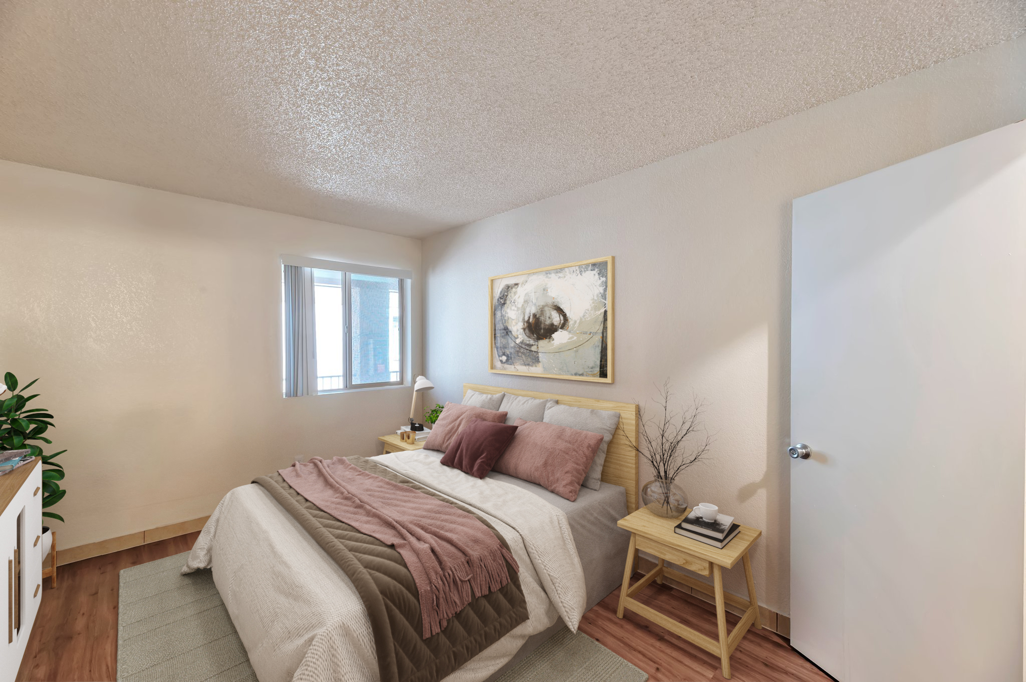 A cozy bedroom featuring a double bed with light bedding and decorative pillows. There are two bedside tables with lamps, a piece of abstract wall art, and a plant in the corner. The room has light-colored walls, a window allowing natural light, and a door leading out. The flooring is wooden.