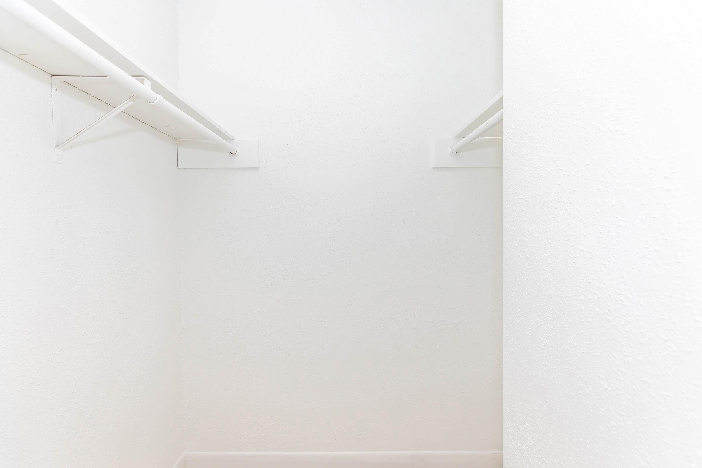 A clean, empty closet with white walls and two hanging rods. The space is well-lit and minimalistic, giving a sense of openness.