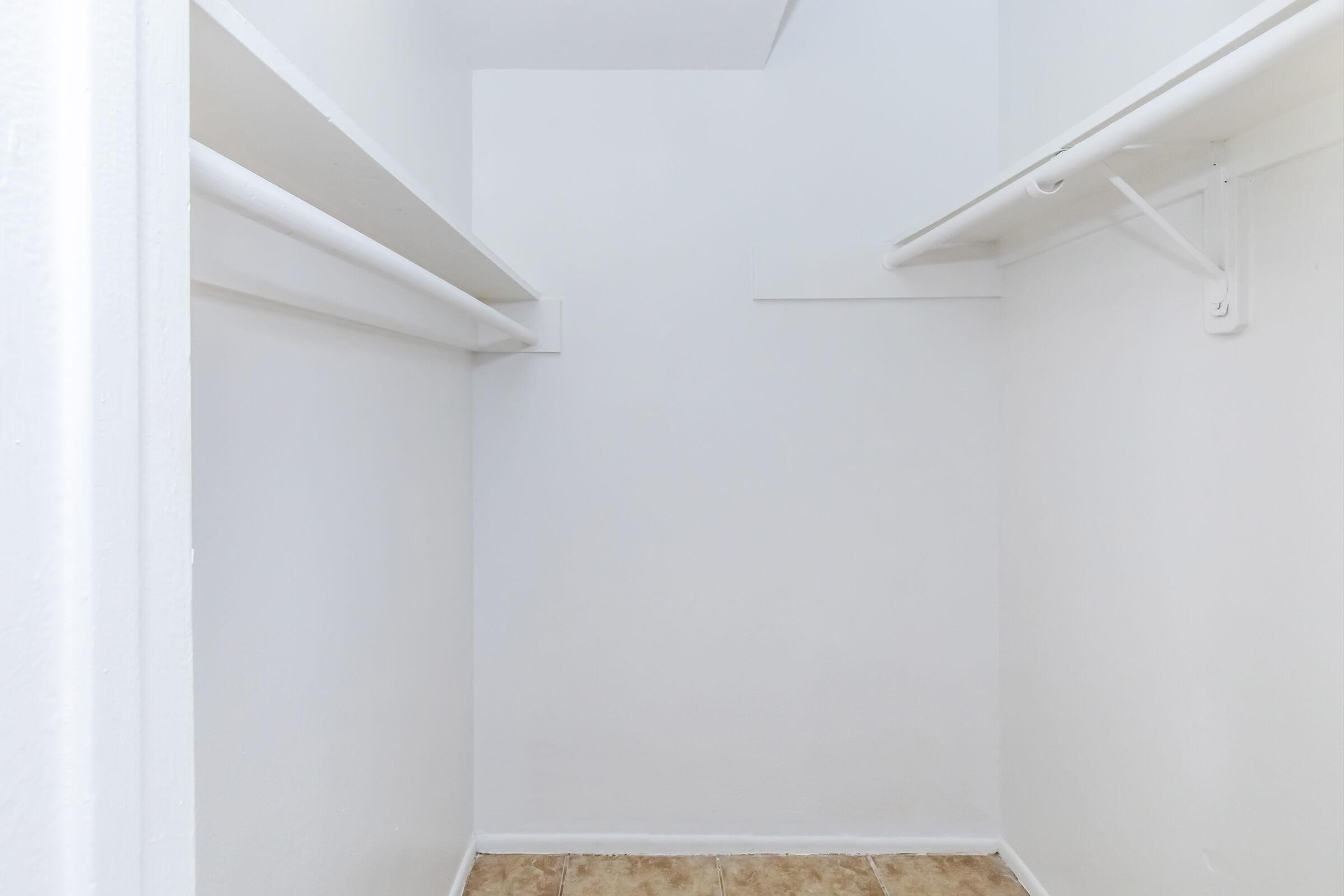 Empty closet with white walls and two hanging rods. The floor is tiled in a light color, and the overall space appears minimalistic and organized.