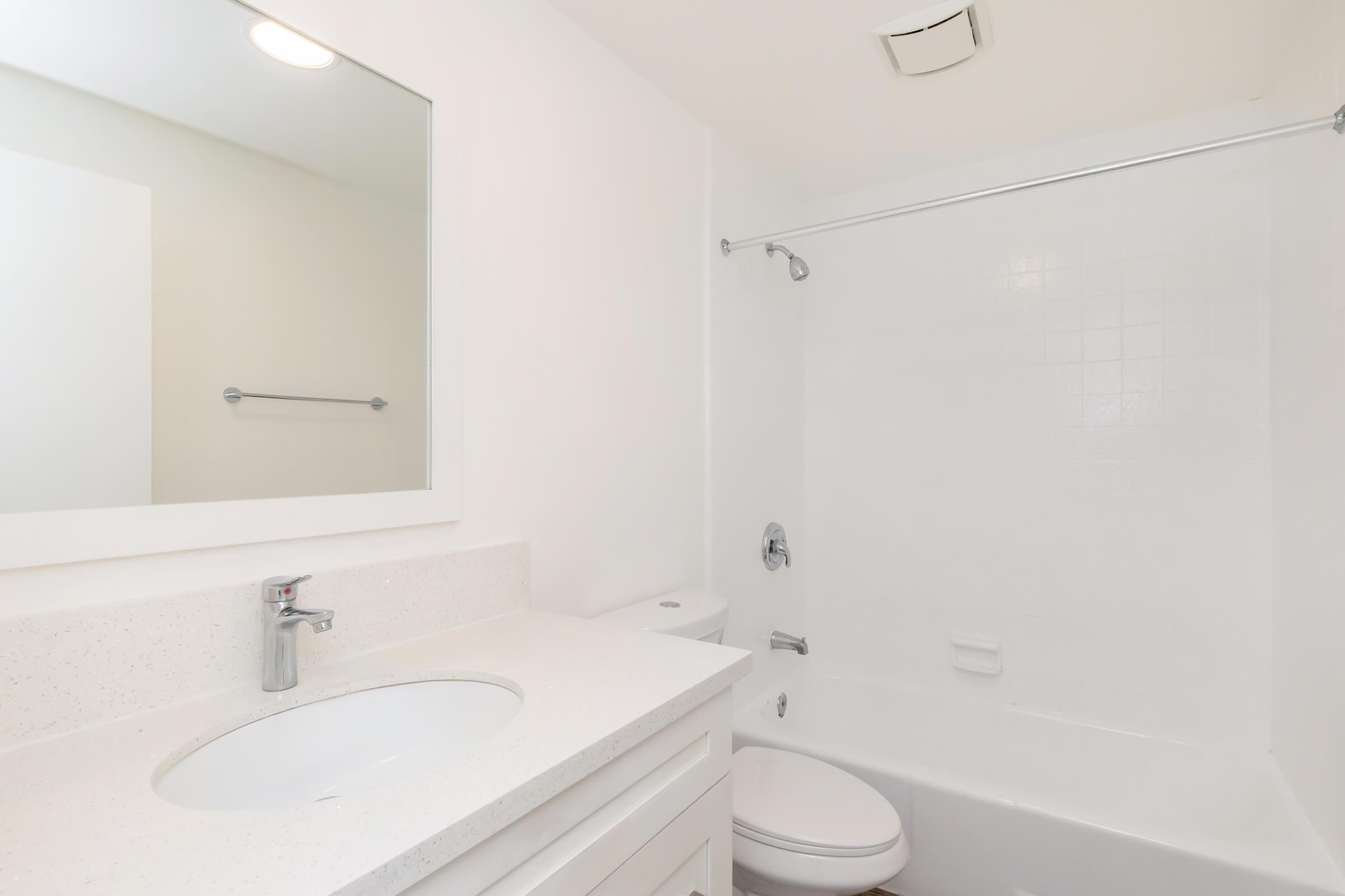 A clean and modern bathroom featuring a white sink with a mirror above, a white bathtub with a shower, and light-colored walls. The design is minimalistic with a bright and airy feel.