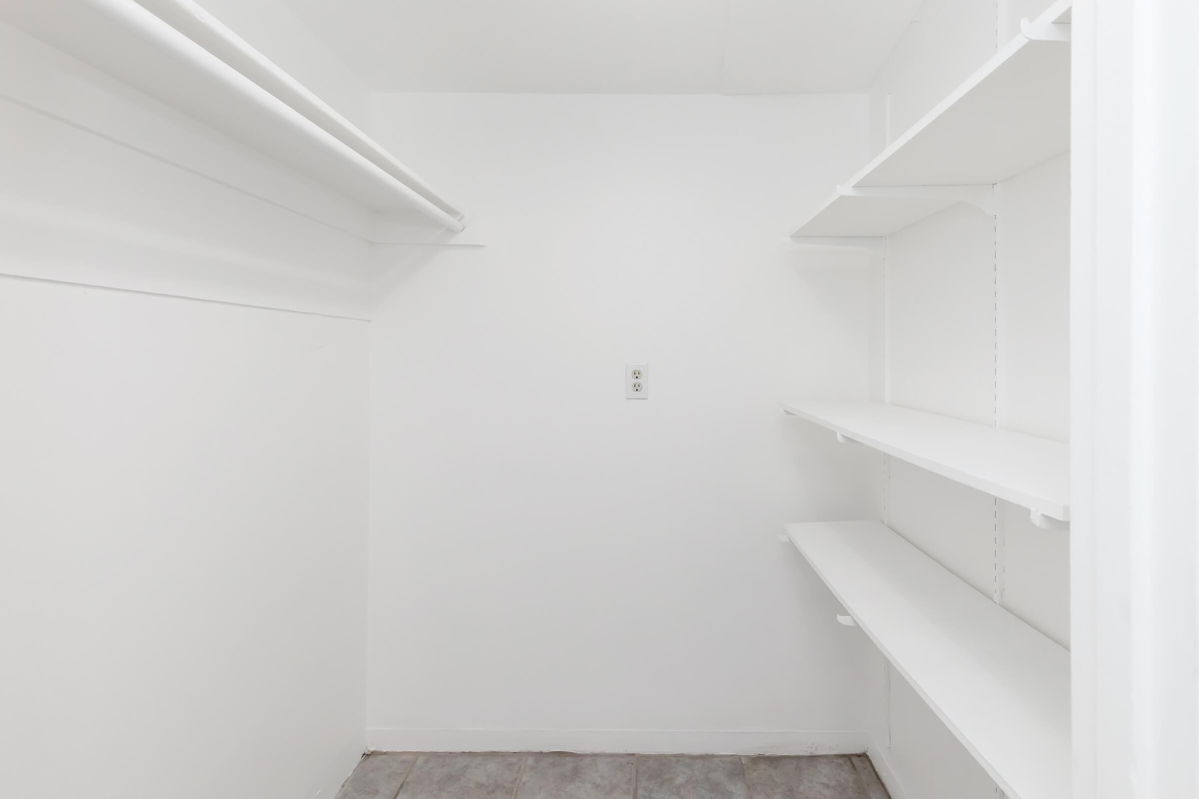 Empty closet or pantry space featuring white walls, one electrical outlet, and two shelves. The floor is tiled, and the overall setting is clean and minimalistic.