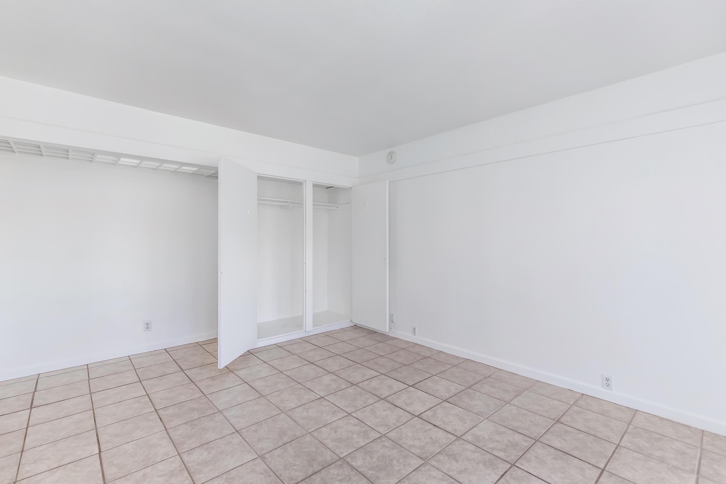 Empty room with white walls, tiled floor, and a closet with sliding doors. The space is well-lit, featuring a minimalist design with no furniture or decorations.