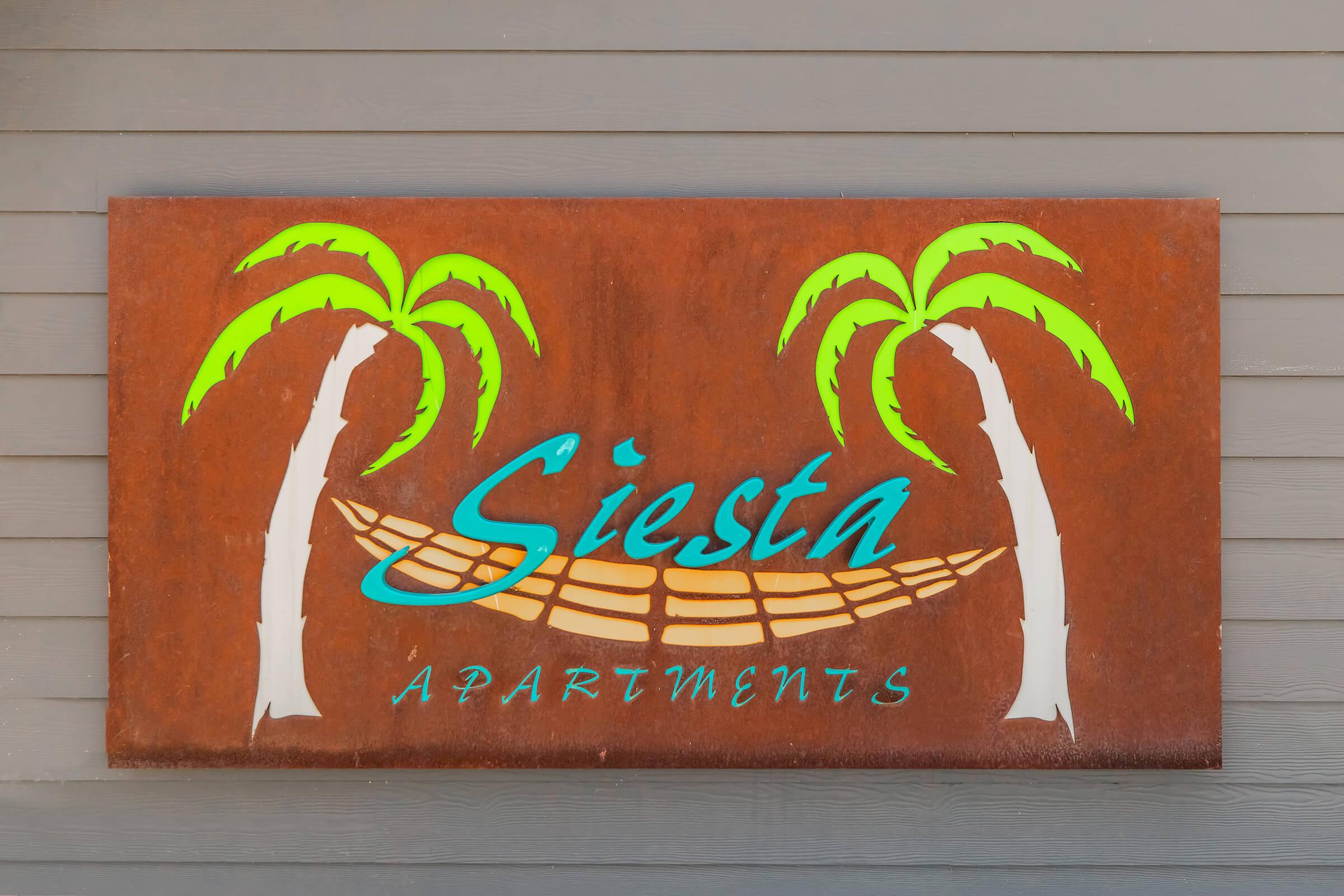 A rust-colored sign featuring the text "Siesta Apartments" in a stylish blue font, flanked by two vibrant green palm trees. The sign has a background that suggests a tropical vibe, with a hammock design incorporated beneath the text.