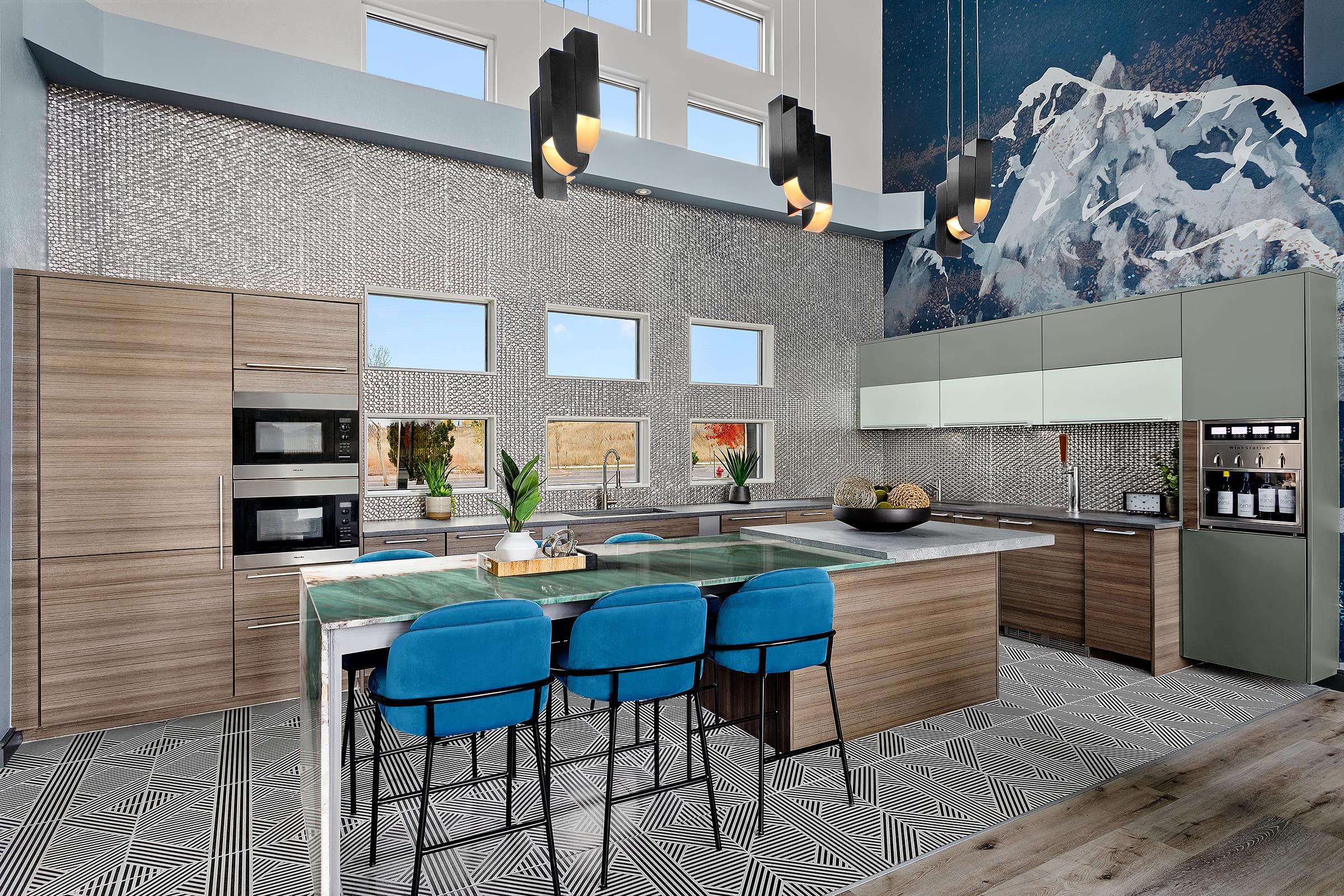 Modern kitchen featuring a large island with a green countertop and blue stools. The cabinets have a mix of wood and green finishes, with built-in appliances and a sleek design. High ceilings, large windows providing natural light, and a mountain mural accentuate the space, complemented by geometric patterned flooring.