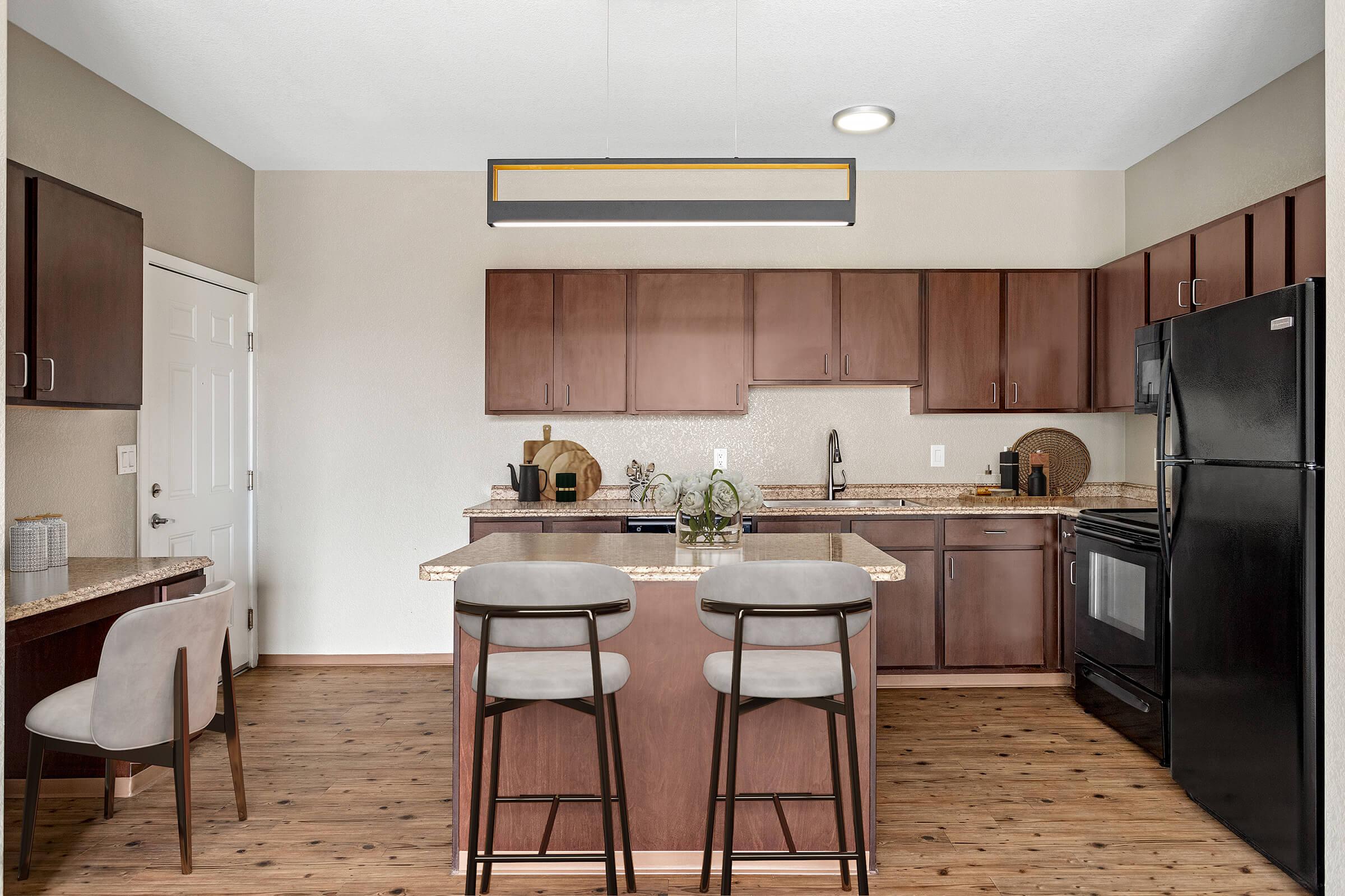 Modern kitchen featuring dark wood cabinets, a center island with seating for two, and granite countertops. The space includes stainless steel appliances, a black refrigerator, and a stylish light fixture overhead, with neutral walls and a warm wooden floor.