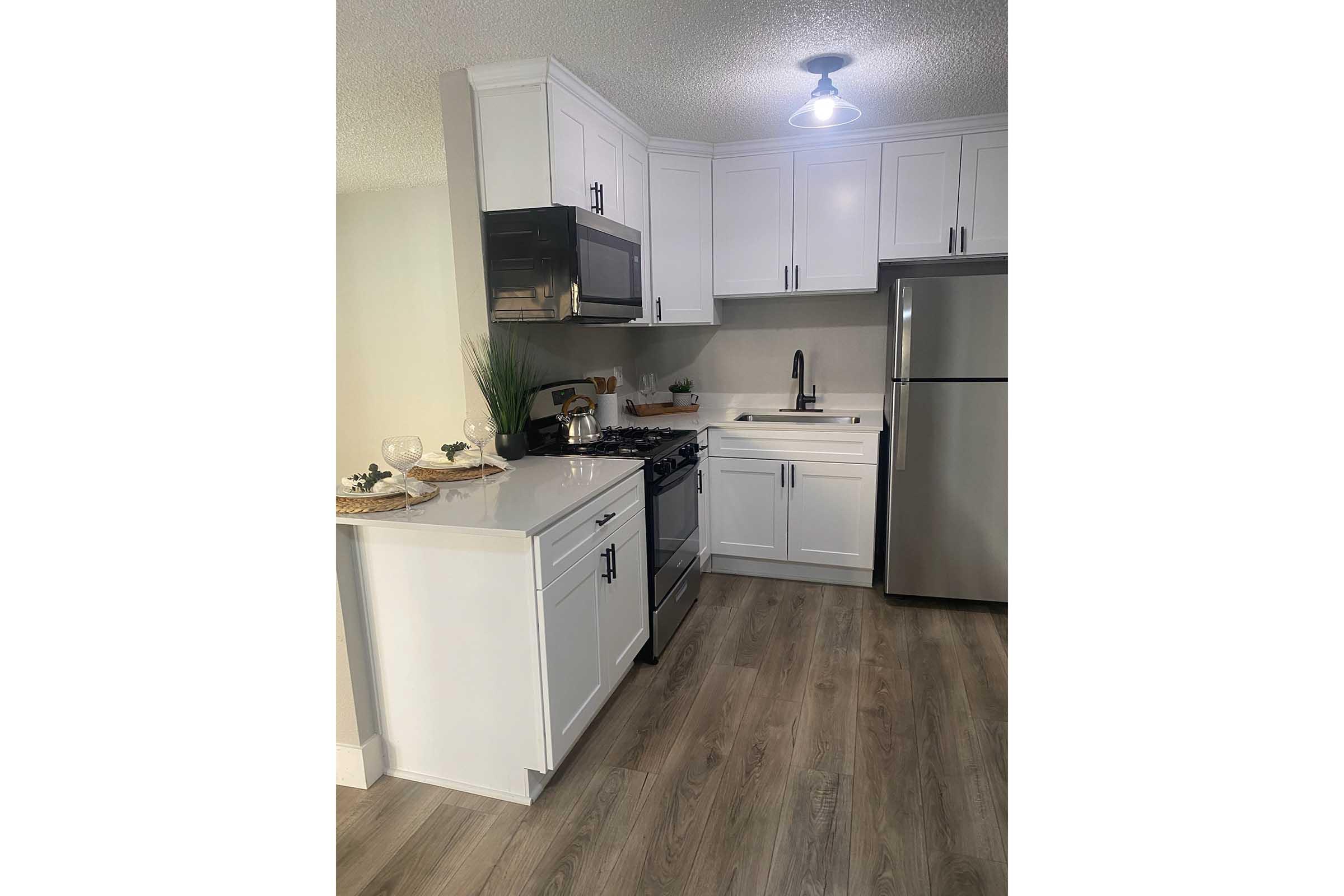 Modern kitchen featuring white cabinets, stainless steel appliances, and a sleek countertop. The layout includes a stove, microwave, sink, and refrigerator. Soft lighting illuminates the space, complemented by a stylish wooden floor and decorative items on the counter.