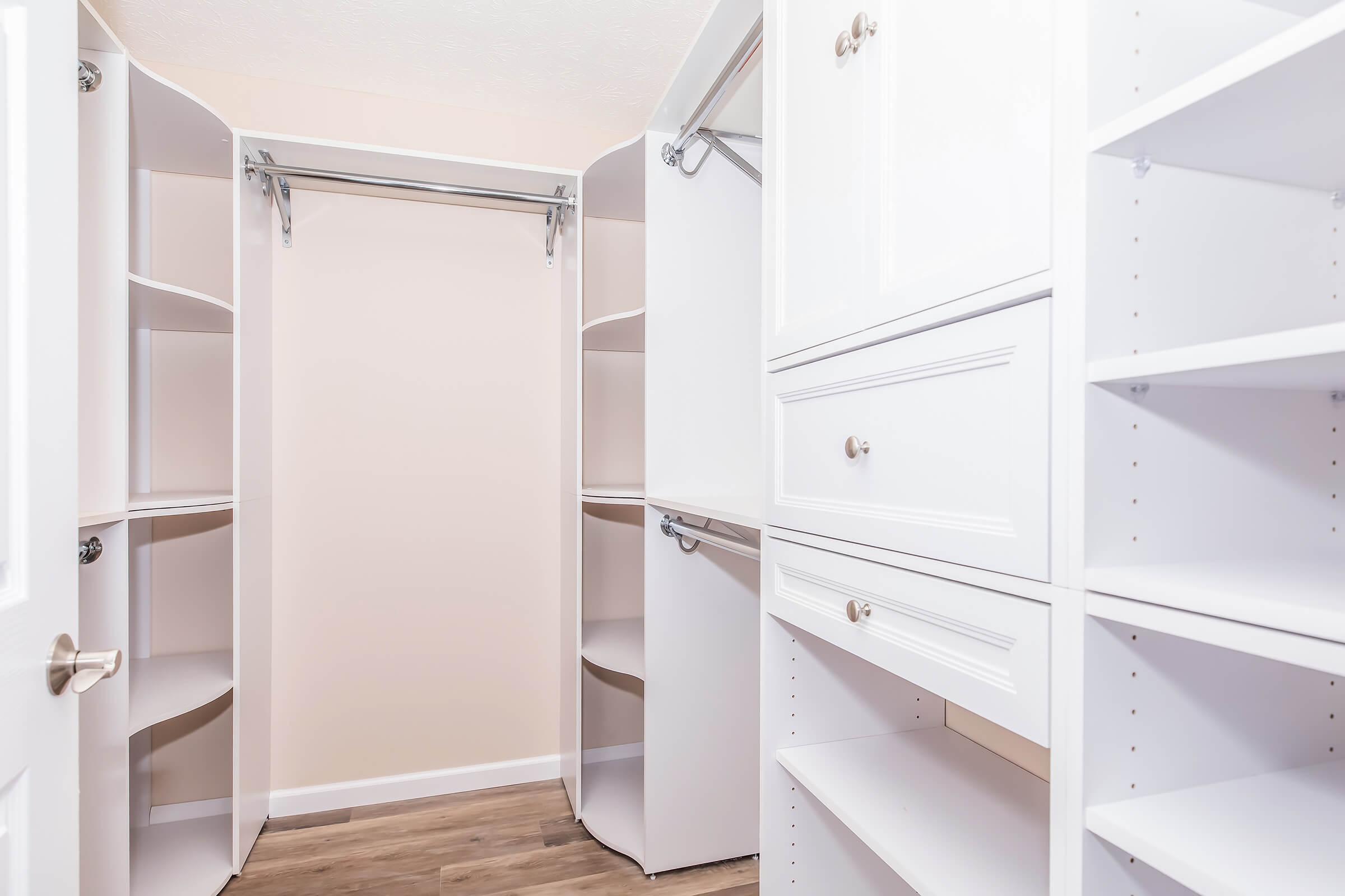 A well-organized closet featuring white built-in shelves, a hanging rod, and drawers. The design includes rounded corners and a light color scheme, creating a spacious and tidy appearance. Bright lighting enhances the visibility of the shelving and storage areas.