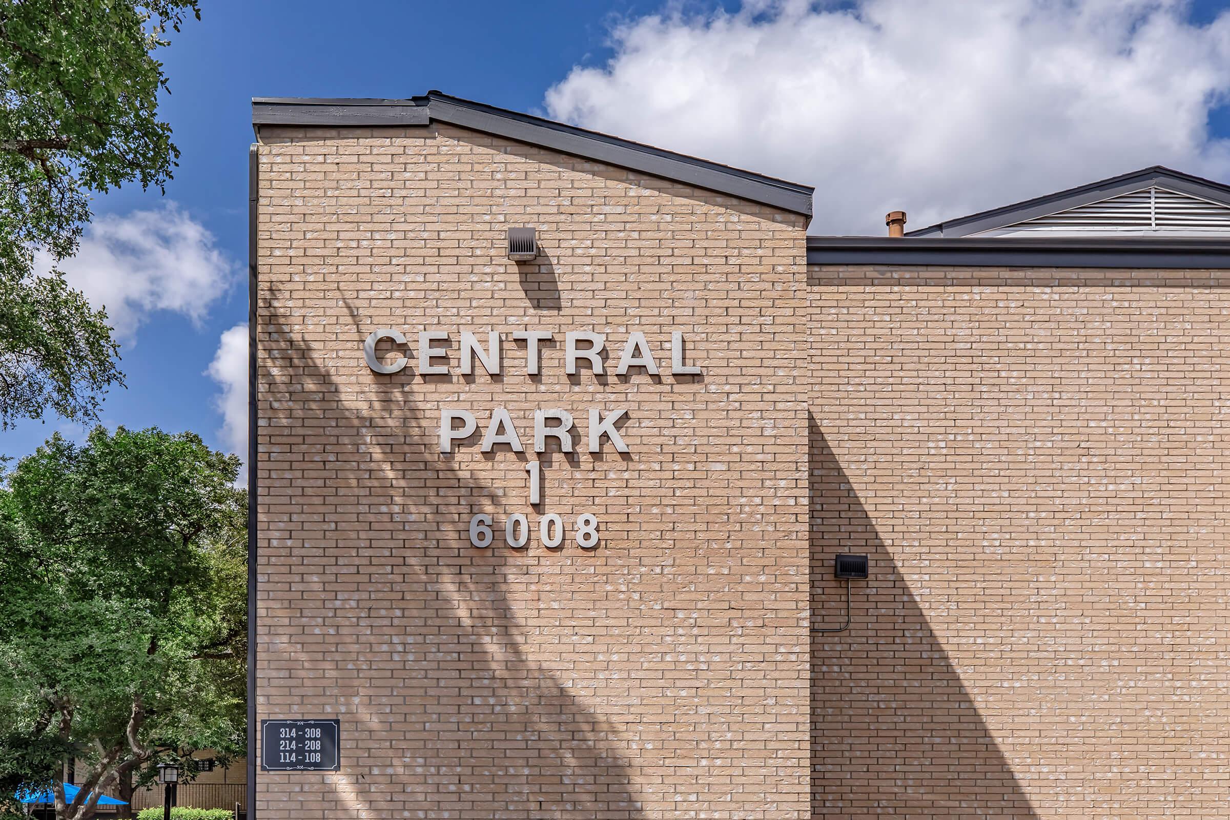 A close-up of a brick building facade featuring the words "CENTRAL PARK" and the number "6008" prominently displayed. The scene is bright, with a clear sky and some trees visible in the background, creating a pleasant outdoor atmosphere.
