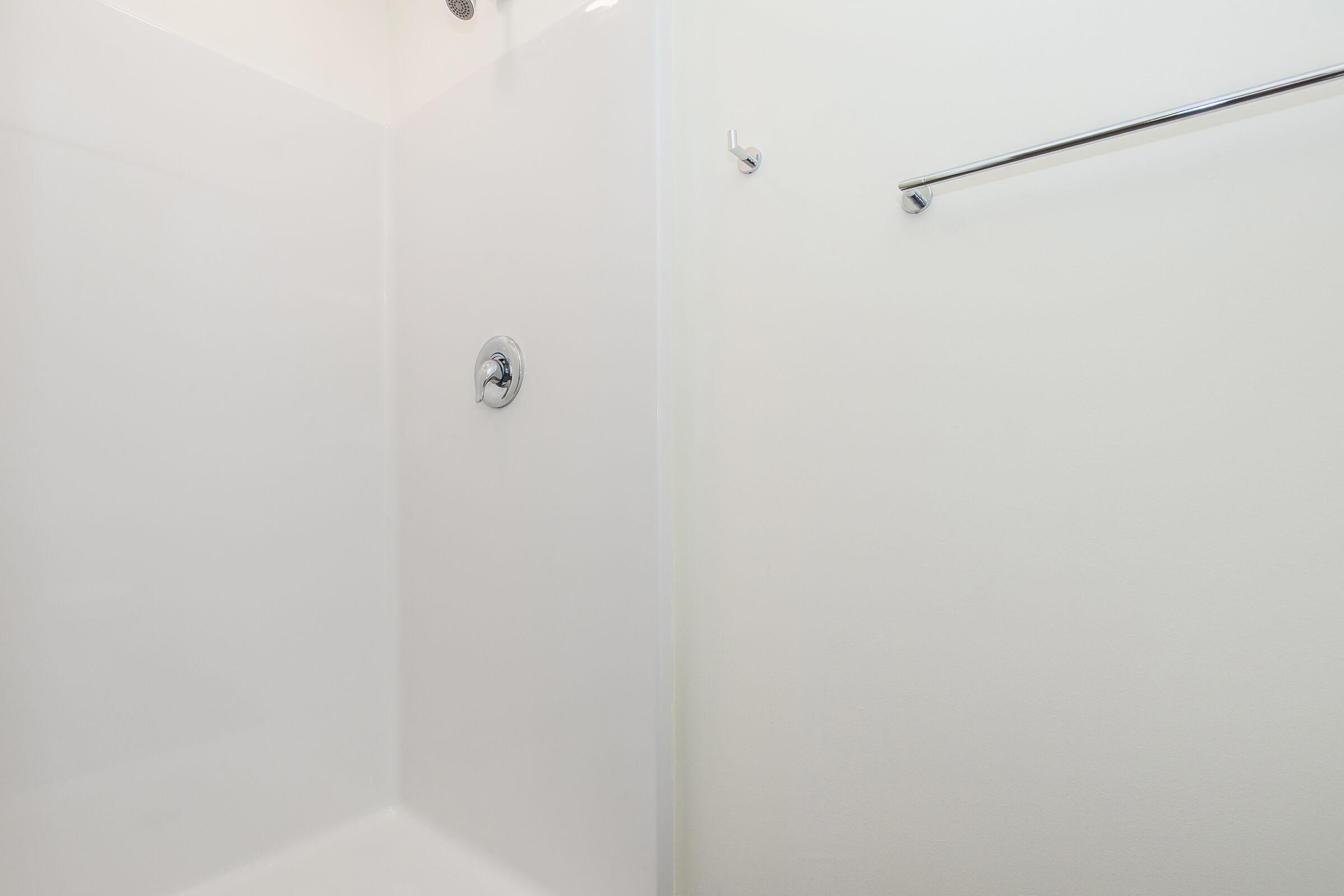 A clean and modern shower stall featuring a white interior, a chrome faucet, and a wall-mounted towel bar. The design emphasizes simplicity with smooth surfaces and minimal decoration, creating a bright and open atmosphere. The shower area is empty, highlighting its fresh and uncluttered appearance.