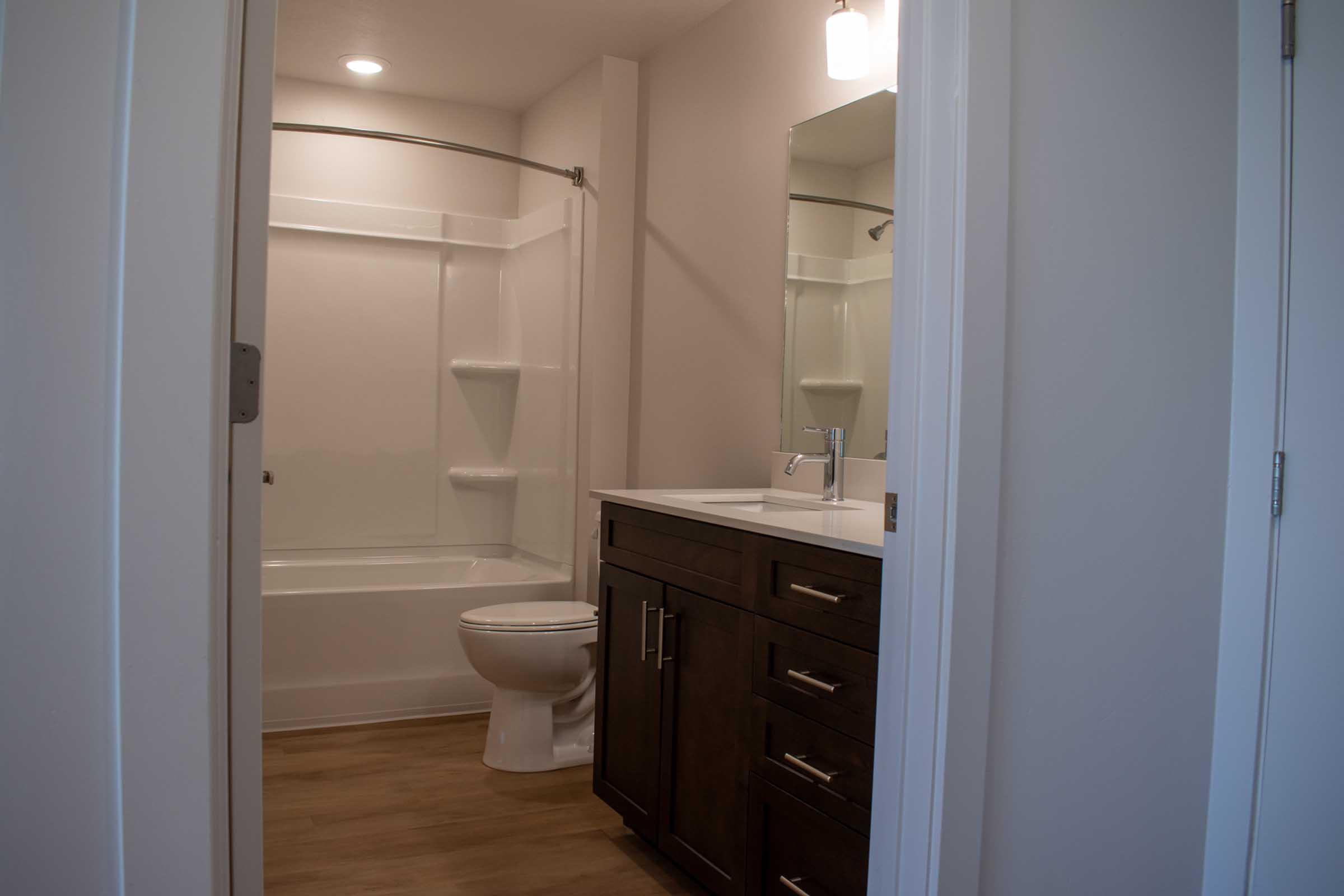 A clean and modern bathroom featuring a shower-tub combo, a single vanity with dark wood cabinets, a white sink, and a toilet. The walls are light-colored, and there's a mirror above the vanity. Soft lighting illuminates the space, creating a bright and inviting atmosphere.