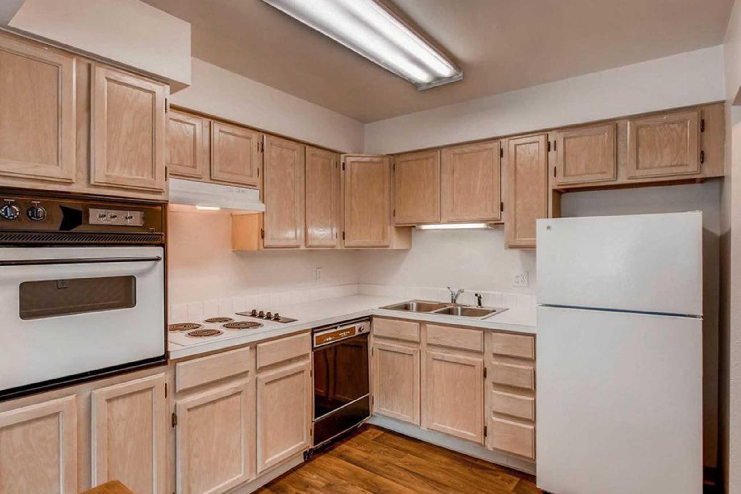 Image of the kitchen interior of apartment home at Royal Garden Apartments. Includes tan cabinets, white refrigerator, black front dishwasher, built in stove top, and white face oven.