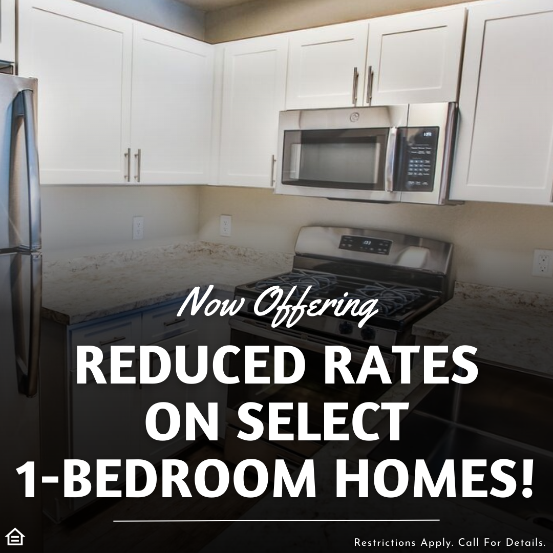 Promotional image set against a background of a bright kitchen with white cabinetry and stainless steel appliances. Large bold text reads: 'Now Offering REDUCED RATES ON SELECT 1-BEDROOM HOMES!' with a disclaimer at the bottom reading: 'Restrictions Apply. Call For Details.'