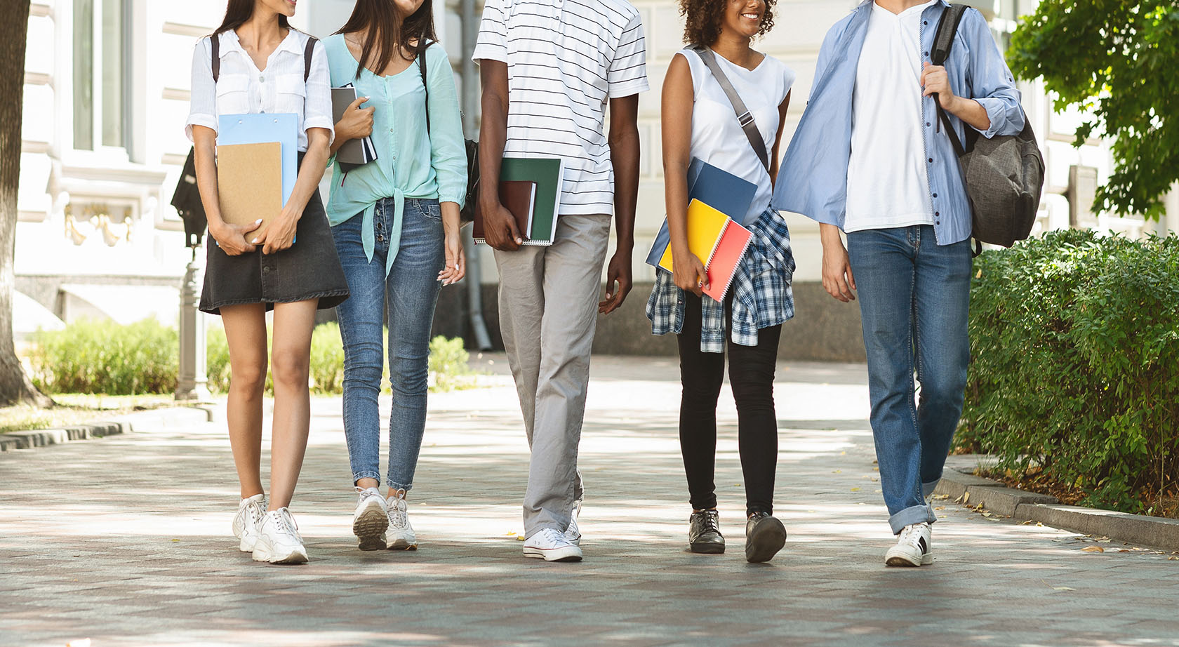 A group of students holding books and walking on a sidewalk