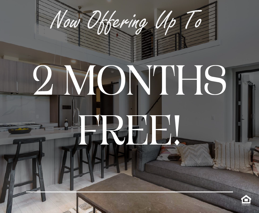 Modern open-concept living space featuring a kitchen with a central island and bar stools, adjacent to a cozy living area with a dark sofa adorned with decorative pillows. A sleek staircase leads to a lofted area above, all set within a bright, minimalist design. The text on the image says, "Now offering up to 2 months free!"