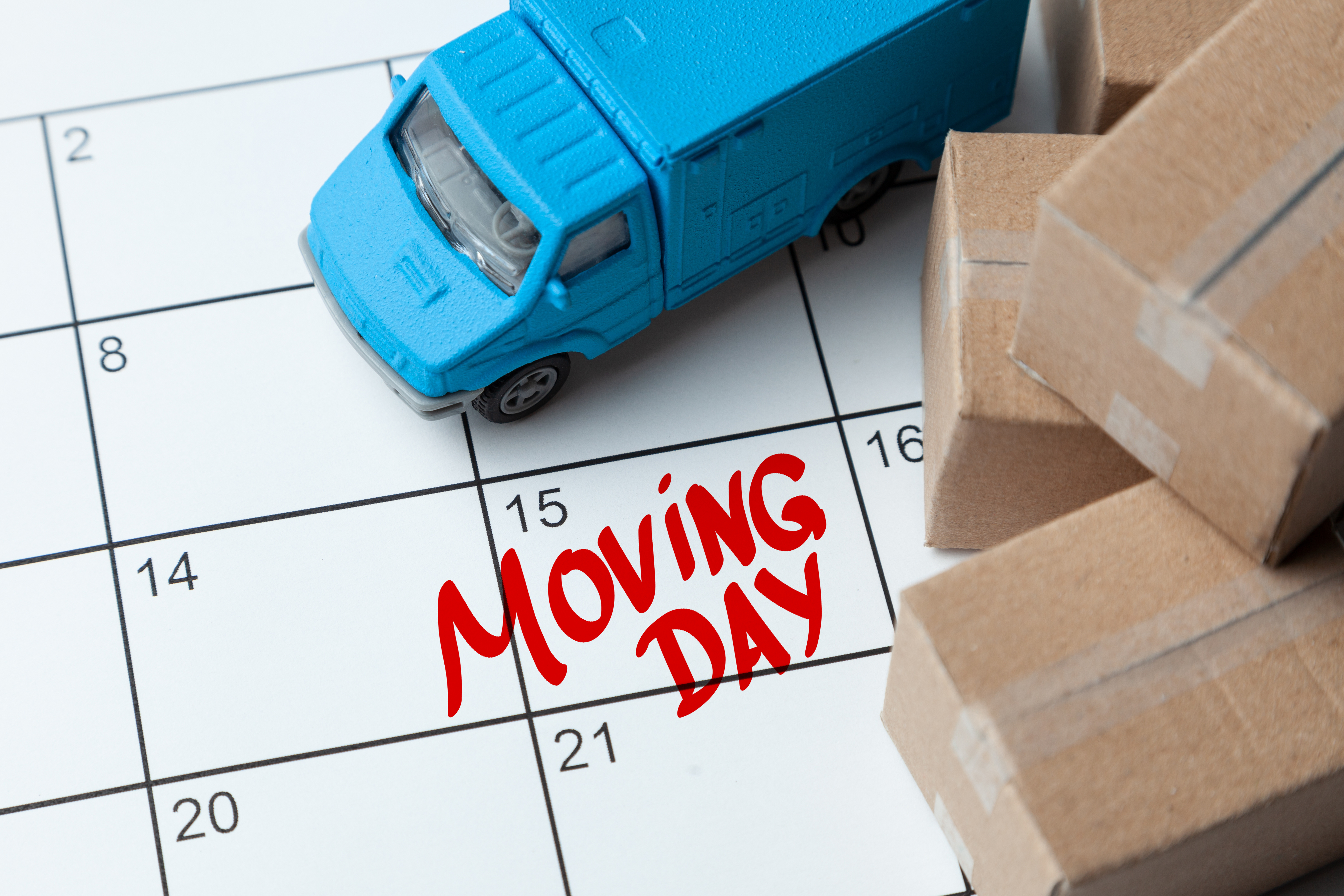 Blue moving truck and brown moving boxes displayed on a white calendar with the words "Moving Day" written in red, illustrating an upcoming apartment move-in date.