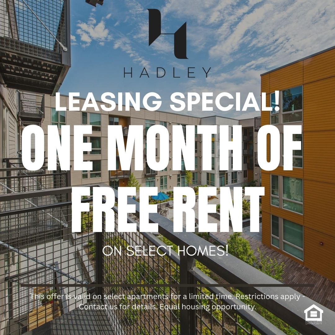 View from a balcony overlooking a modern apartment complex with a central courtyard. The scene features two buildings — one with a light facade and the other with wood accents. Lush greenery and a swimming pool are visible in the courtyard, under a bright blue sky with scattered clouds text reads leasing special one month of free rent on select homes This offer is valid on select apartments for a limited time Restrictions apply Contact us for details Equal housing opportunity