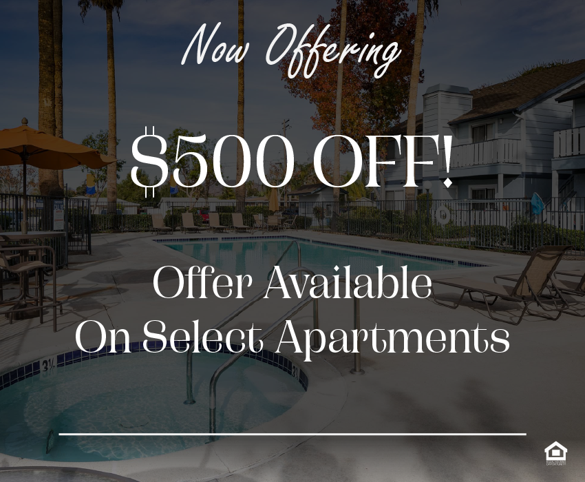 A serene outdoor pool area featuring a clear blue swimming pool and a hot tub. Surrounding the pool are lounge chairs and orange umbrellas, with palm trees and colorful autumn foliage in the background. Nearby, a two-story building can be seen, creating a relaxed atmosphere. The text on the image says, "Now offering $500 OFF! Offer Available On Select Apartments."