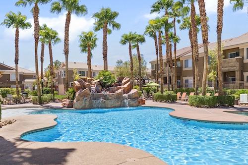 swimming pool with rock waterfall,  palm trees and apartments in the background