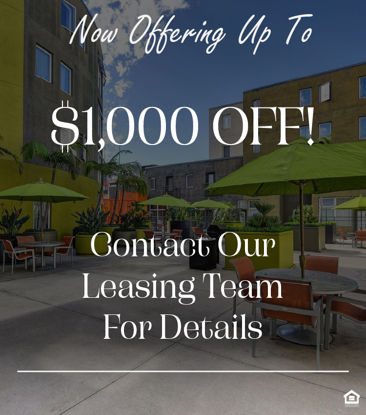 A vibrant outdoor courtyard featuring green umbrellas over patio tables surrounded by plants. The walls of the buildings are a mix of yellow and gray, and there are seating areas for relaxation. The sky is clear with a few clouds, creating a bright and inviting atmosphere. The text on the image says, "Now offering up to $1,000 off! Contact our leasing team for details."