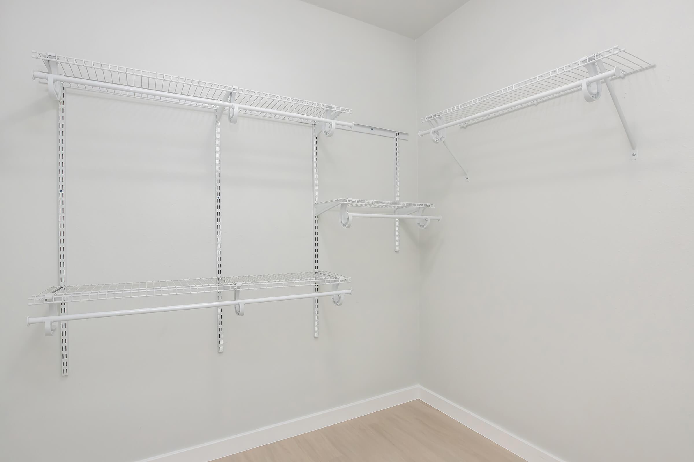 Empty closet with white wire shelving installed on light-colored walls. The design features multiple shelves in a minimalist style, allowing for storage organization. The floor is pale wood, creating a bright and spacious appearance.